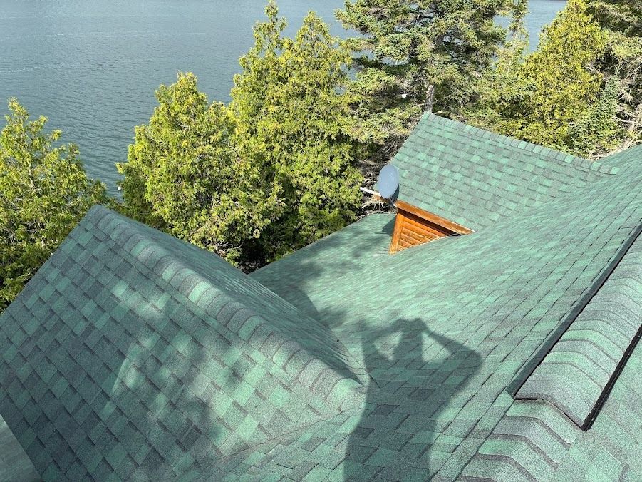 Green shingled cabin roof beside trees and water, with a person’s shadow on the roof
