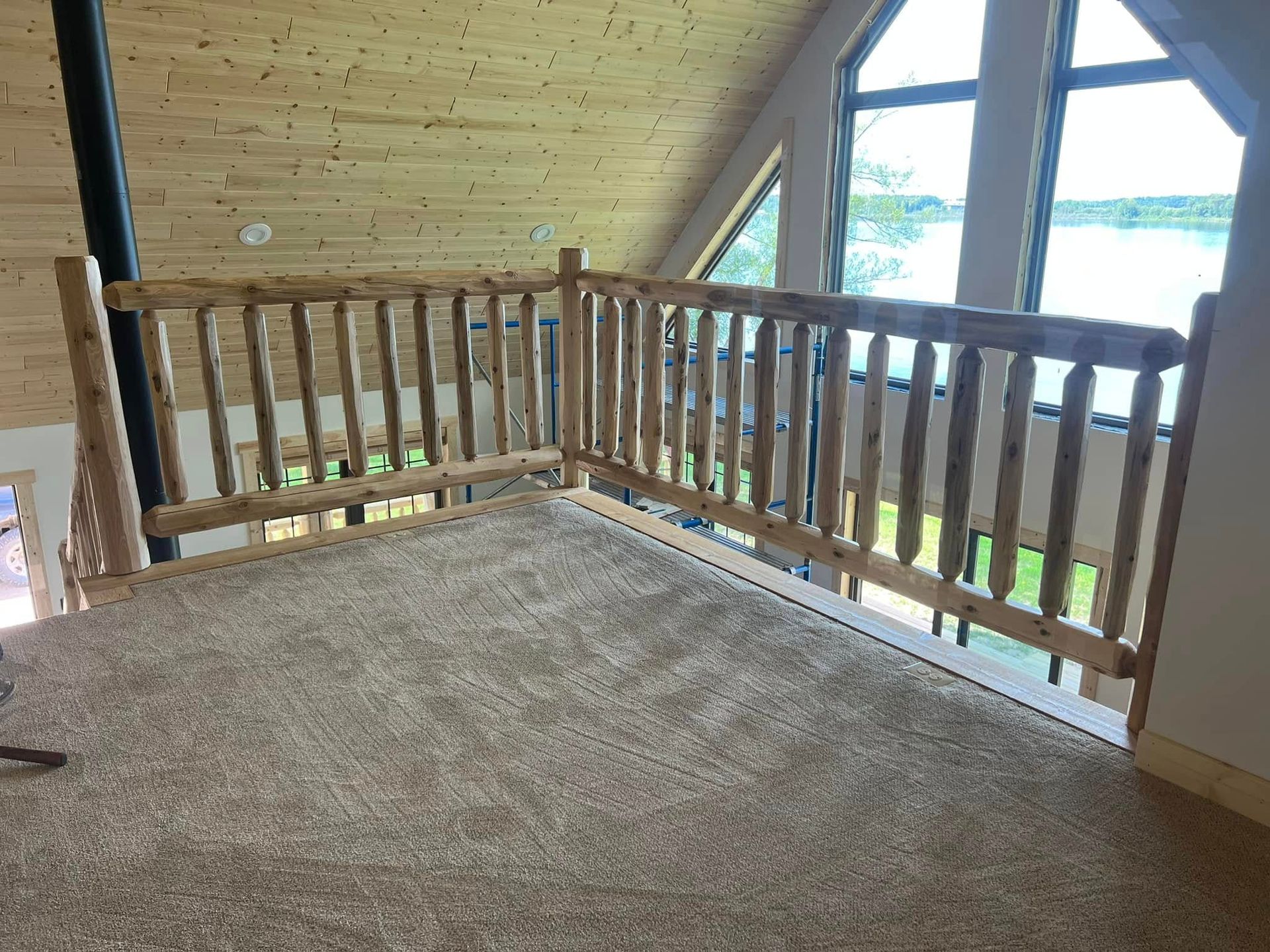 Carpeted loft with wooden railing and large windows overlooking greenery