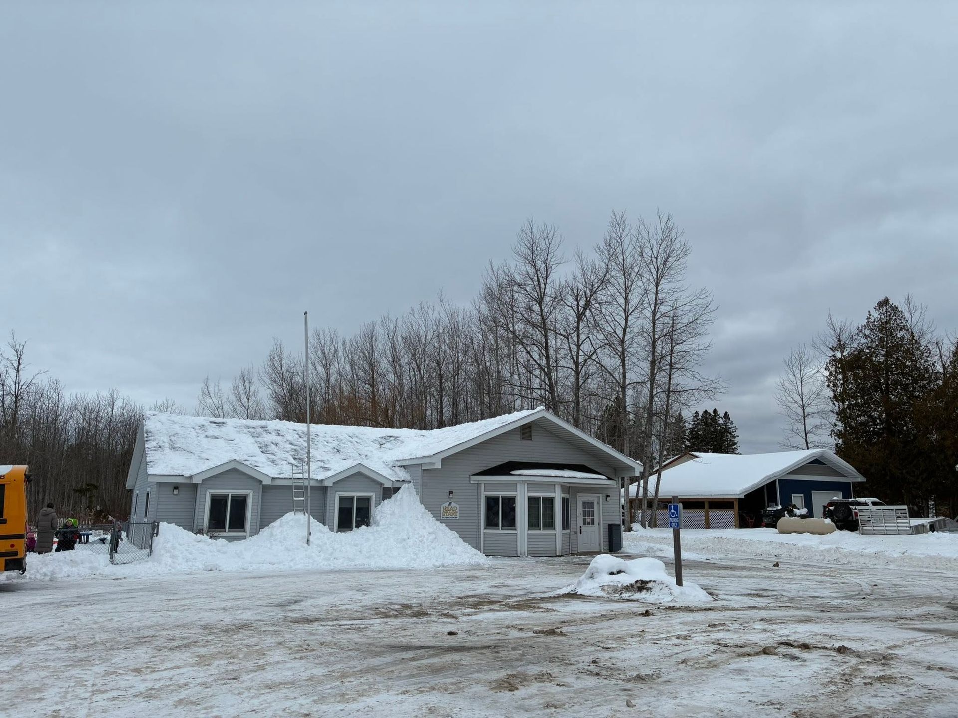 Snow-covered suburban house with a gray roof and trees under an overcast winter sky.
