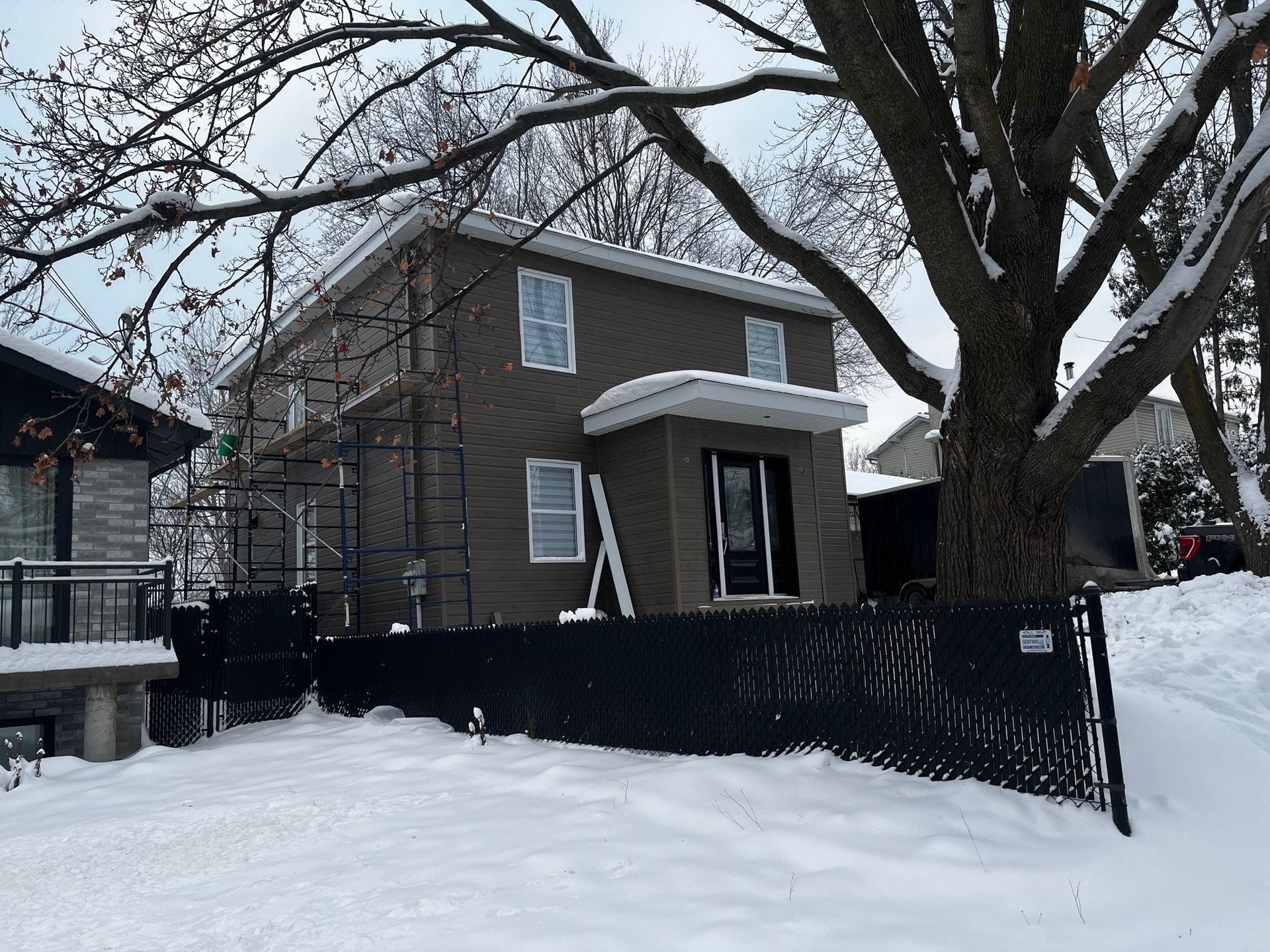Une maison avec une clôture noire et un arbre dans la neige