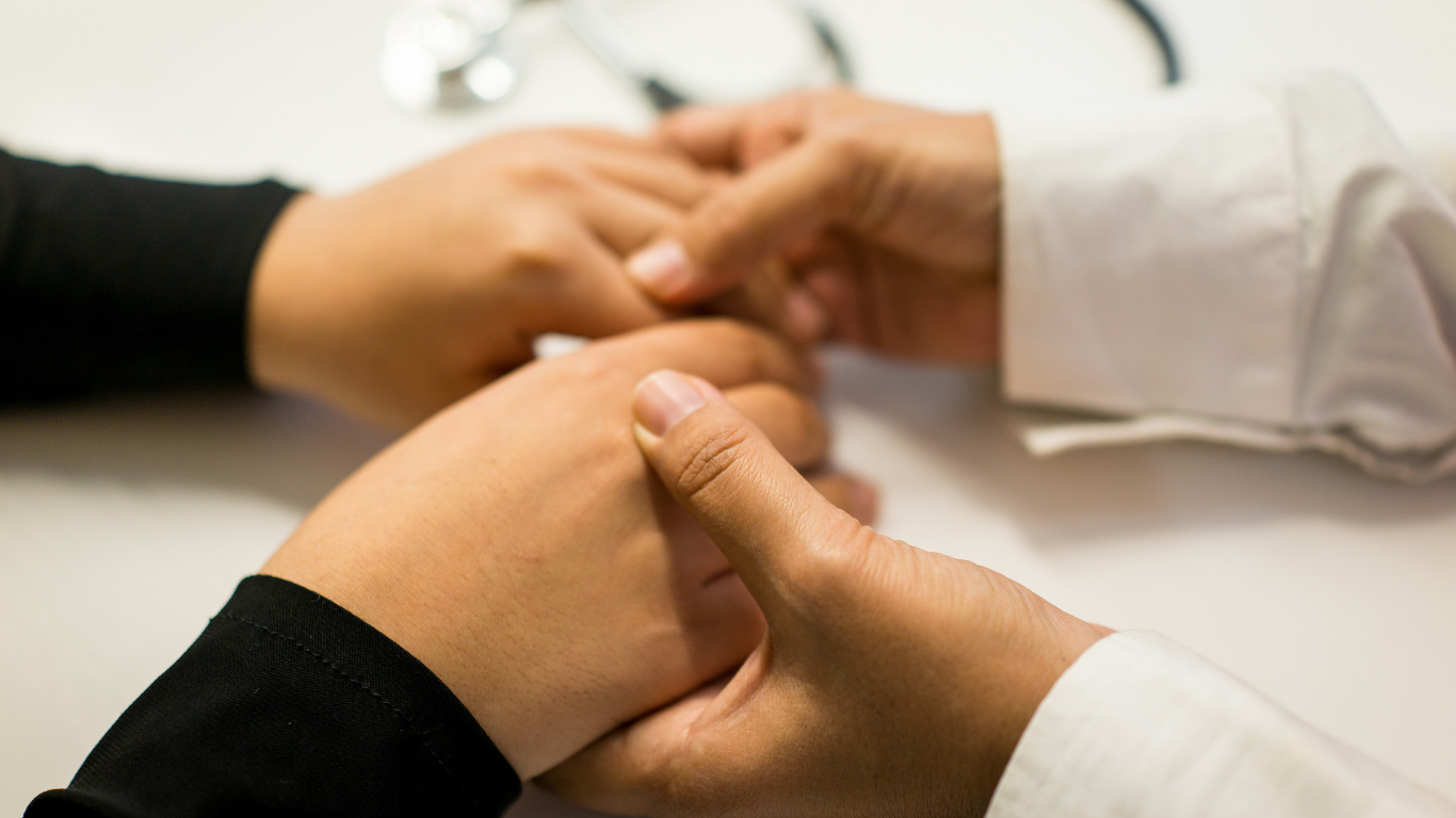 Doctor holding patient's hands, offering comfort. Stethoscope in background.