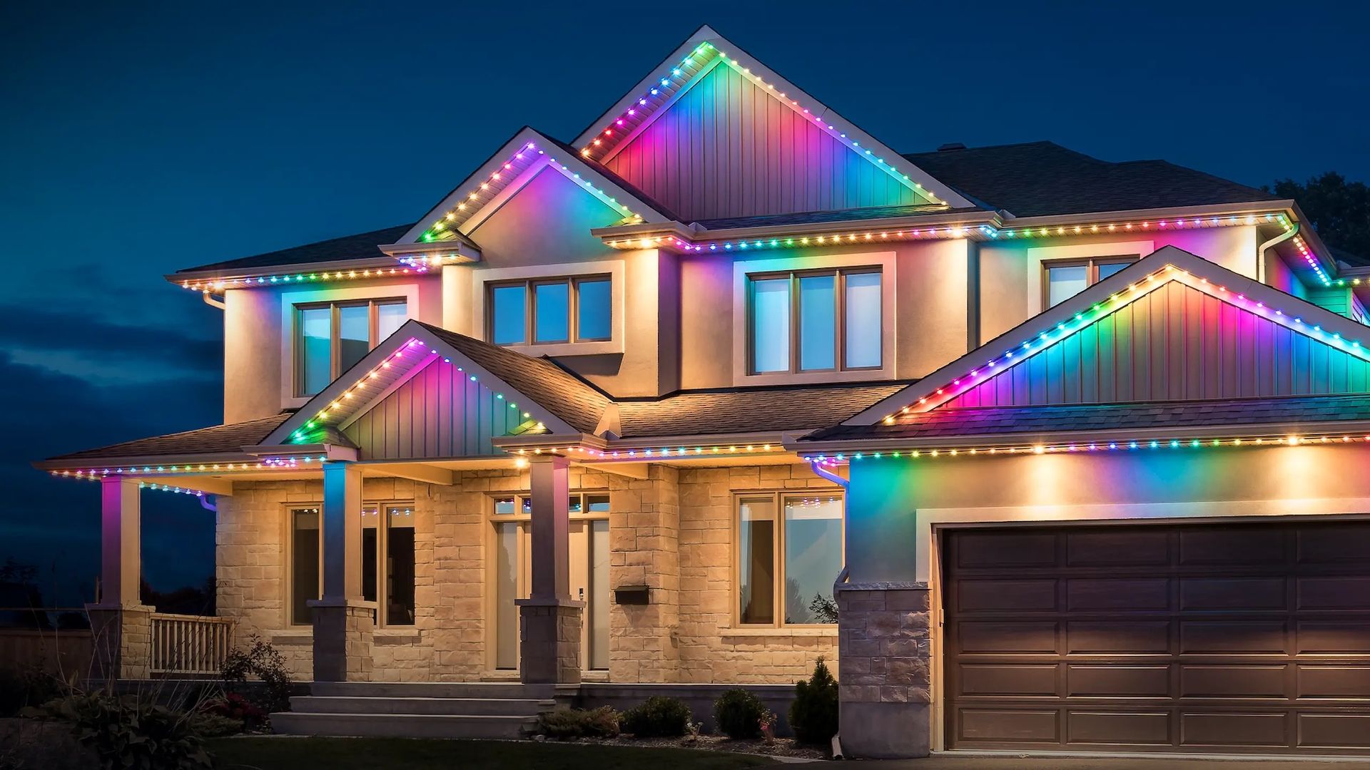A two-story suburban home decorated with vibrant, multi-colored, rainbow-effect LED roofline lights at night.