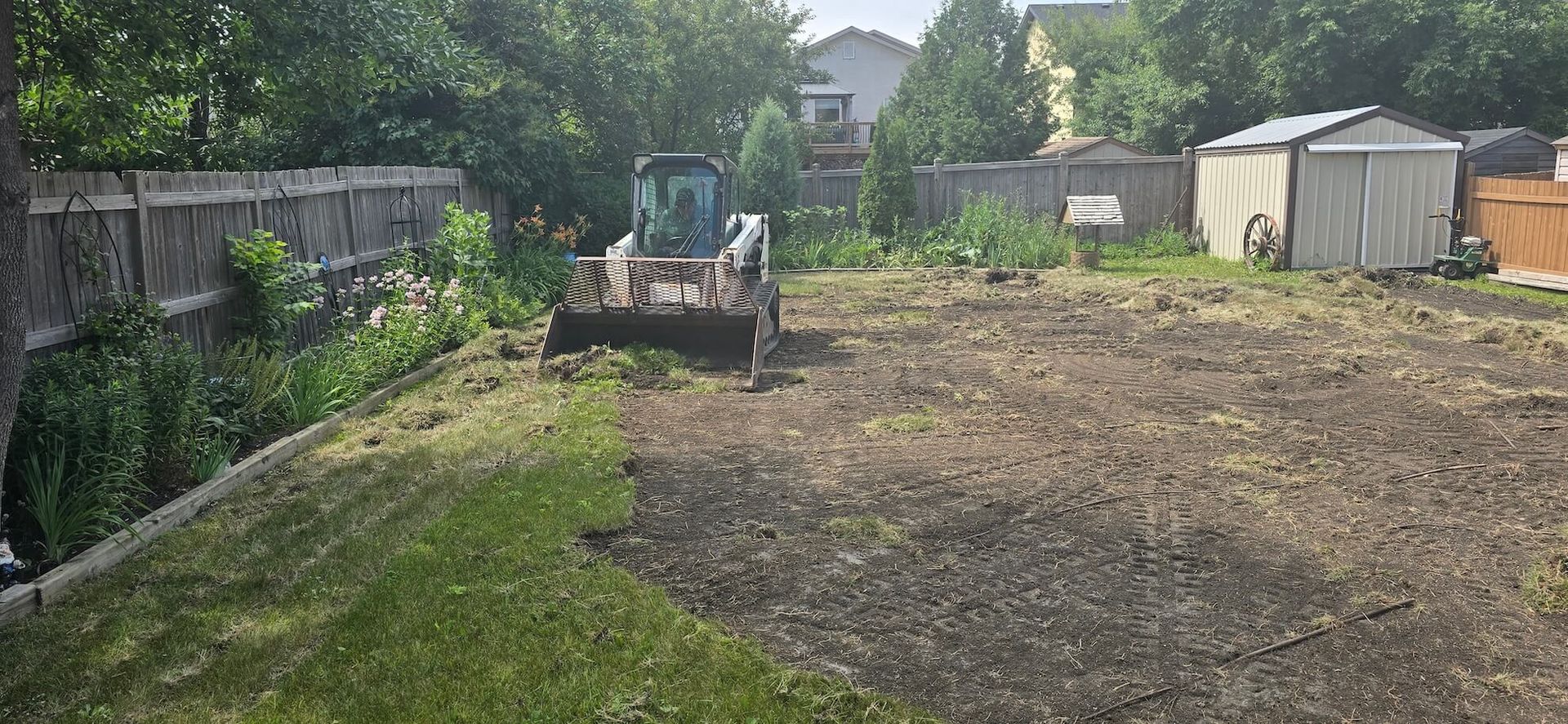 A small bulldozer levels a cleared yard, preparing it for new landscaping.