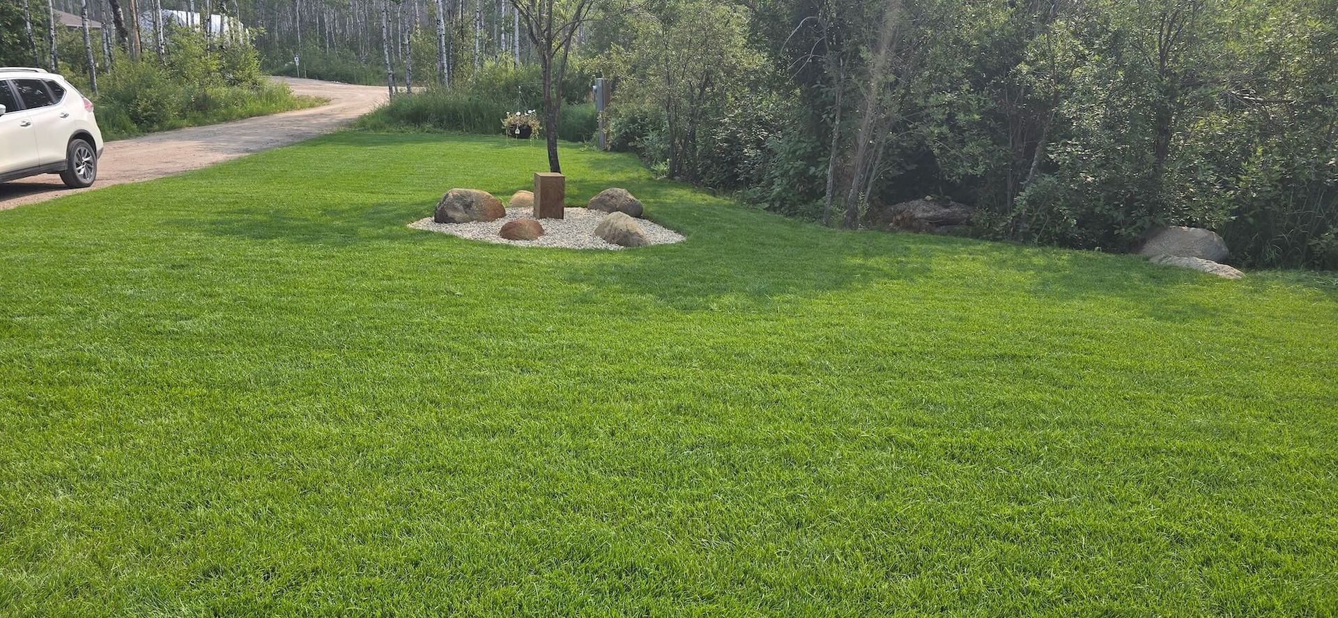 Lush green lawn with a small decorative feature in the center, and a white car parked on the left side of a paved path.
