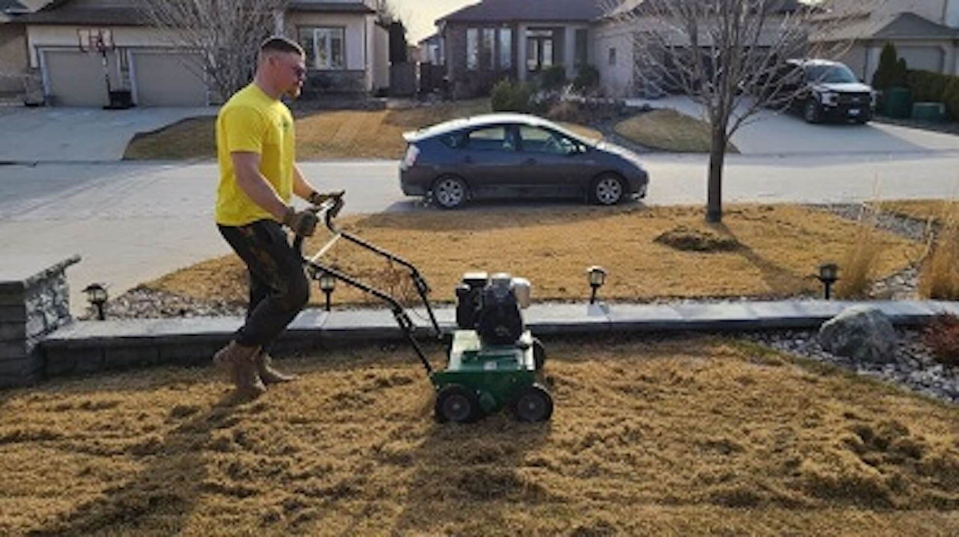 Man operating a lawn aerator in a residential yard. Brown grass, sunny day.