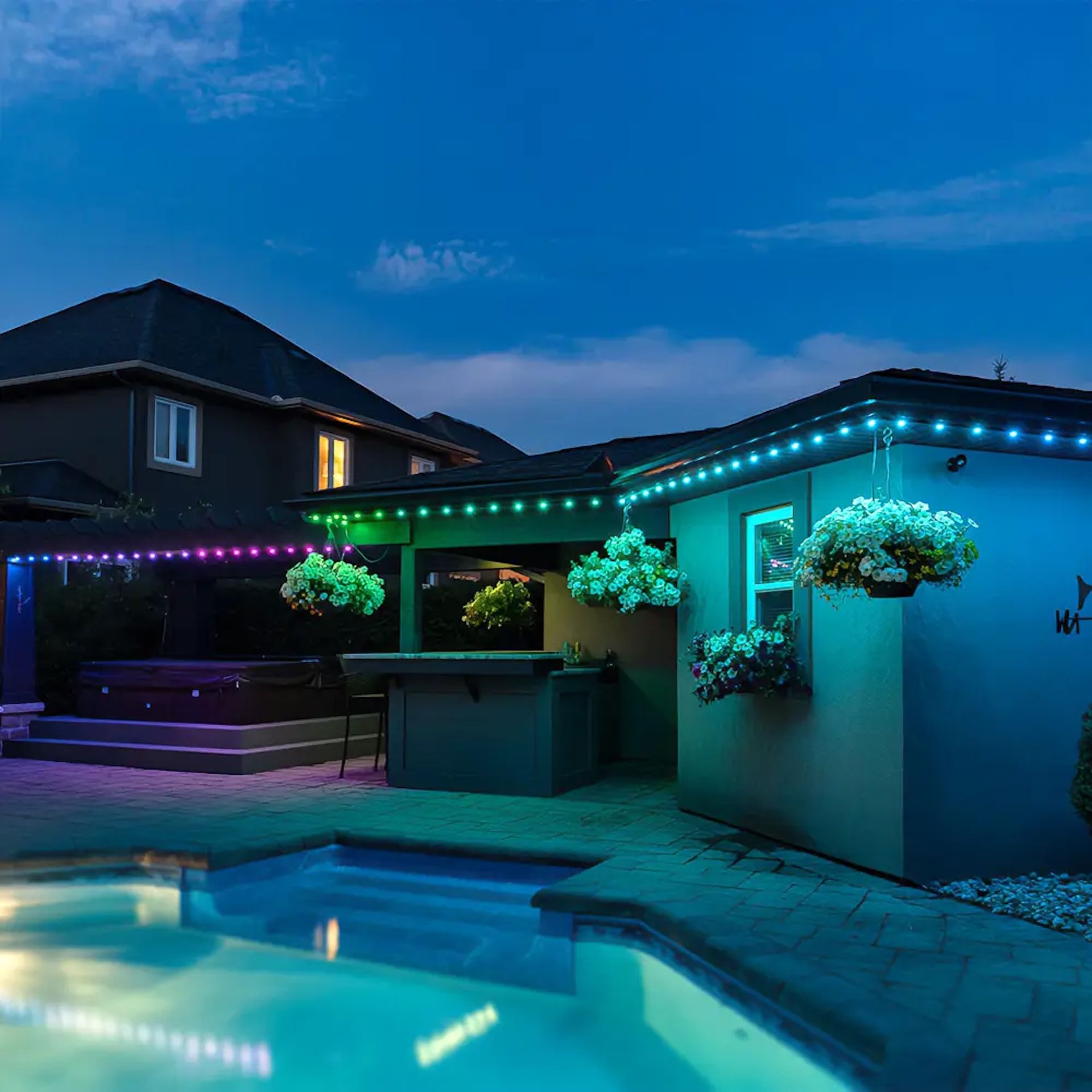 A swimming pool at night, framed by a house illuminated with vibrant blue and purple LED accent lighting.