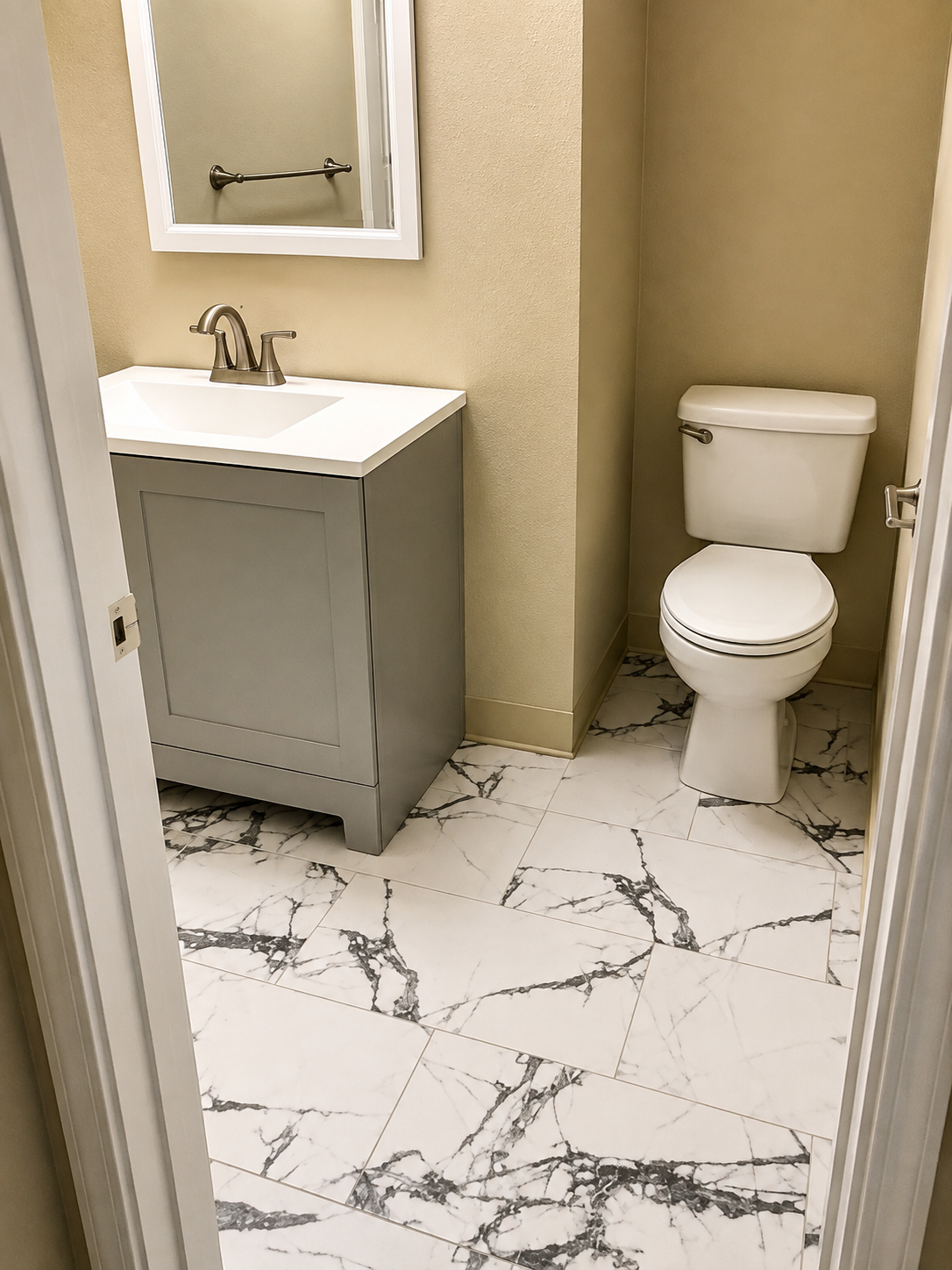 Small bathroom with white vanity, mirror, toilet, and marble-pattern tile floor.