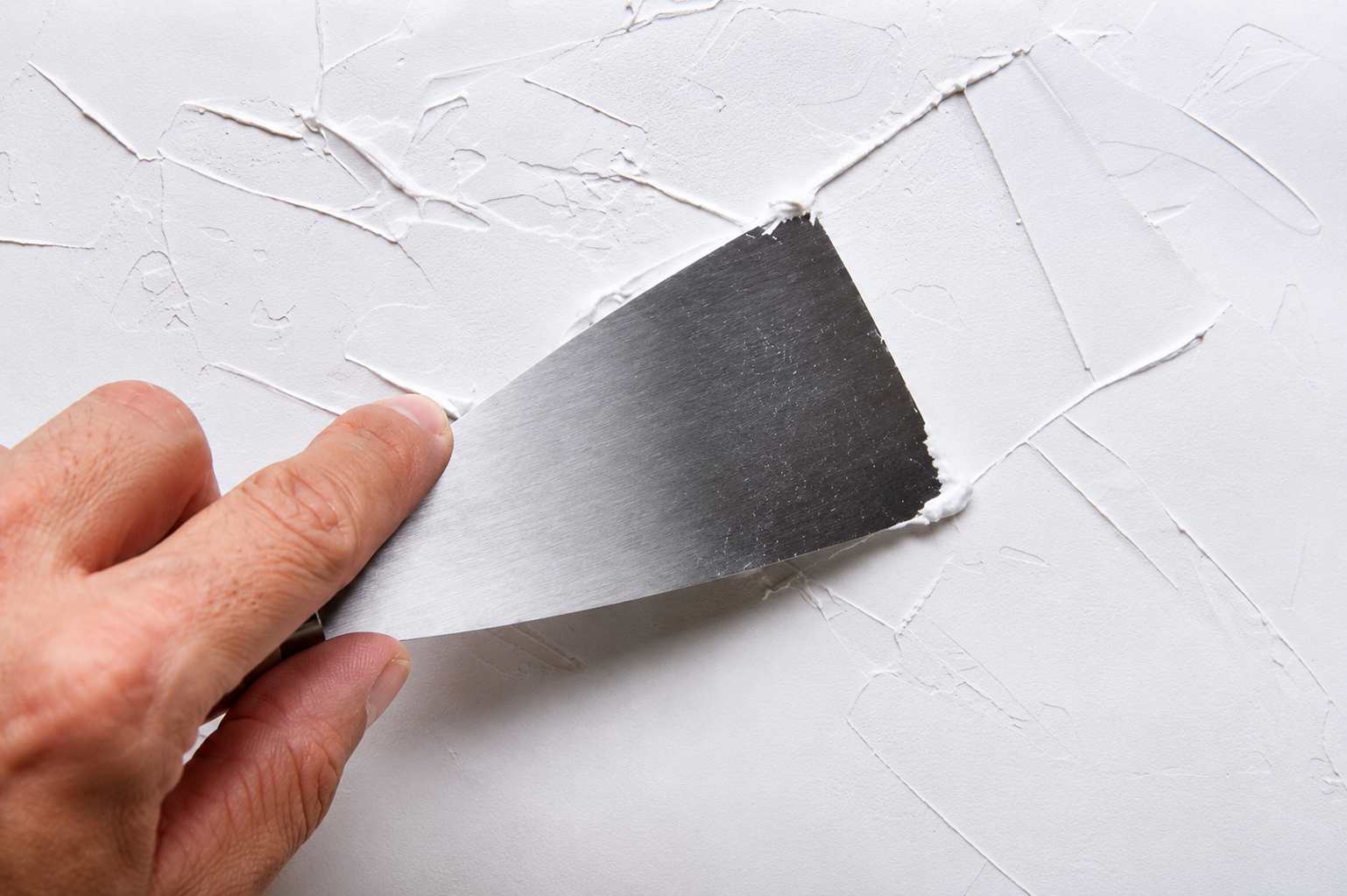 Hand holding a metal putty knife smoothing white plaster on a wall