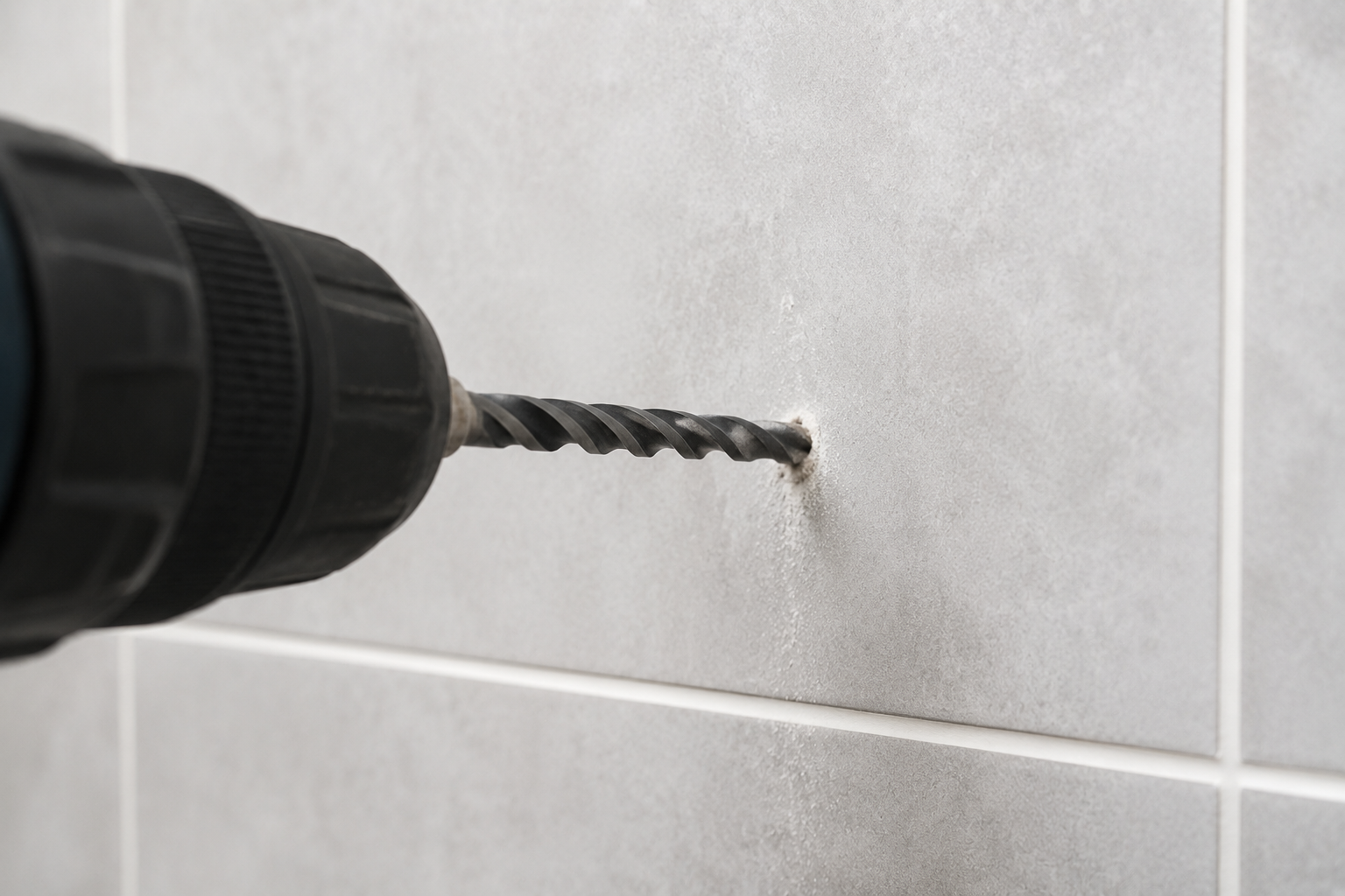 Drill bit boring into a gray tiled wall, creating a hole
