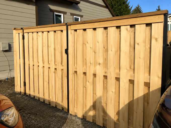 Wooden fence or gate beside a house, with vertical slats and sunlight casting shadows.