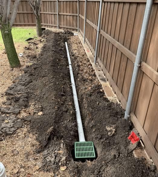 Backyard trench with a white pipe and green drain grate along a wooden fence
