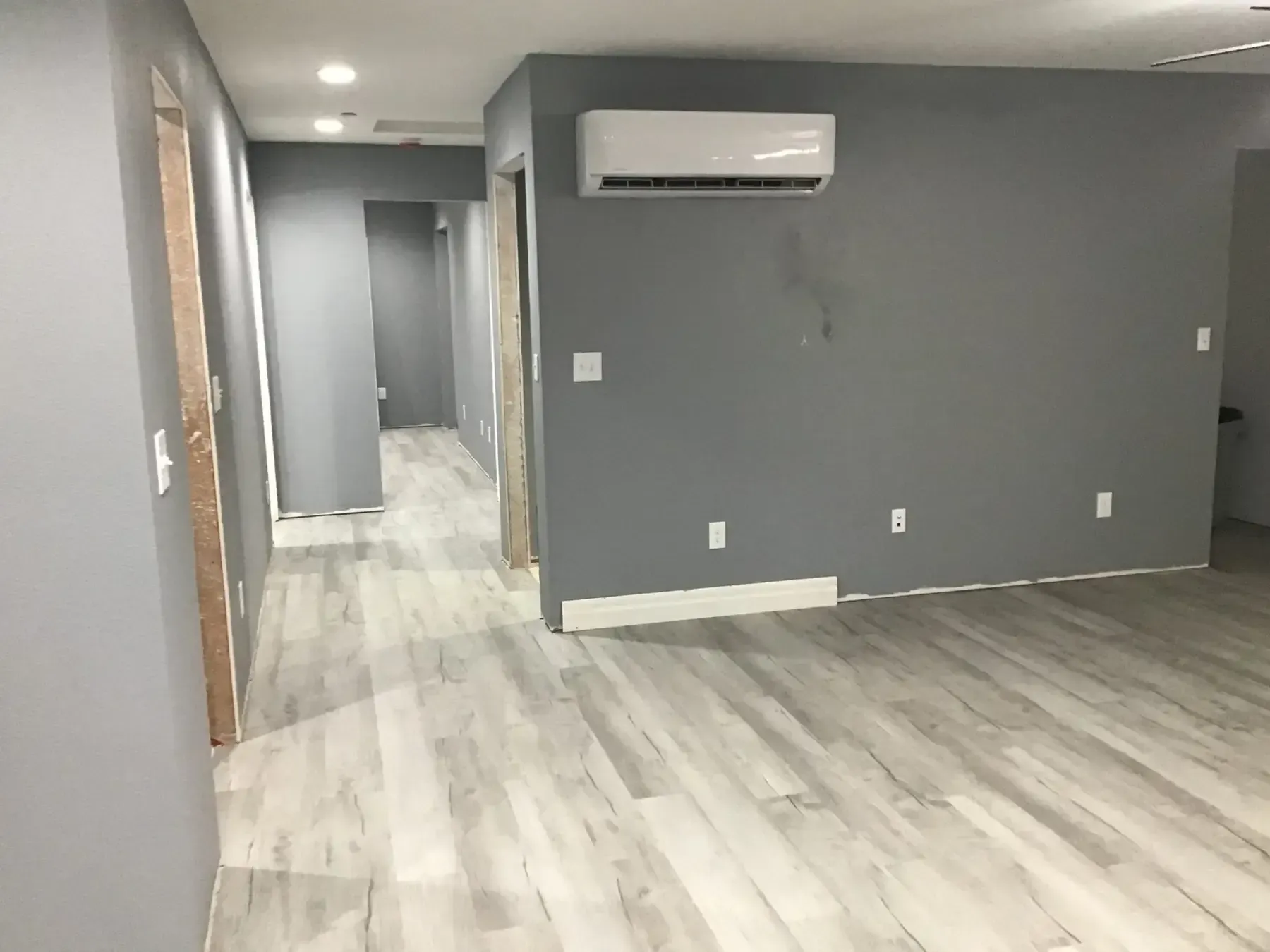 Empty gray room with light wood flooring, hallway, and wall-mounted air conditioner