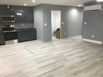 Empty modern kitchen and living area with gray walls, black cabinets, and light wood floors