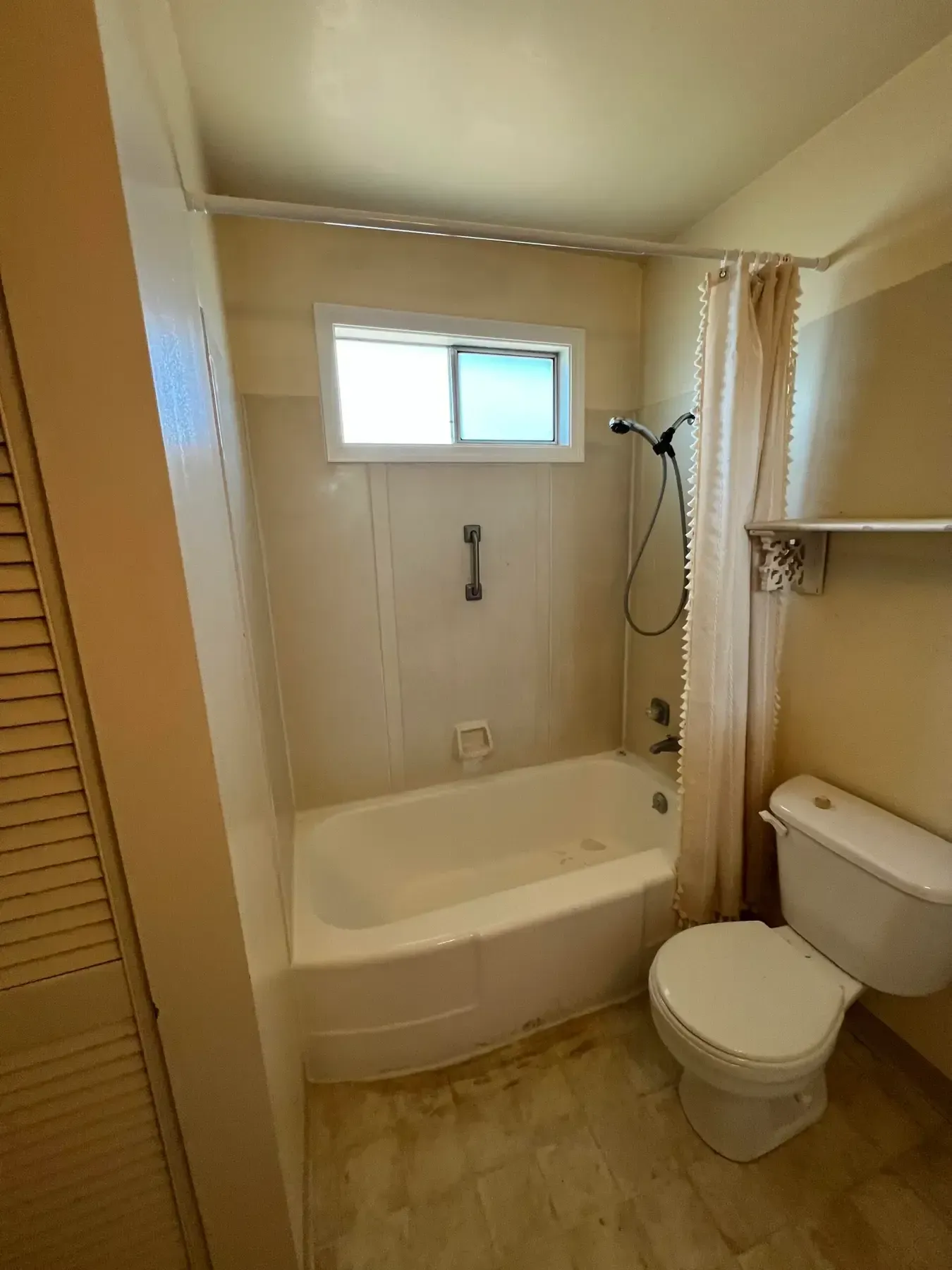 Small beige bathroom with tub-shower, toilet, window, and wall cabinet