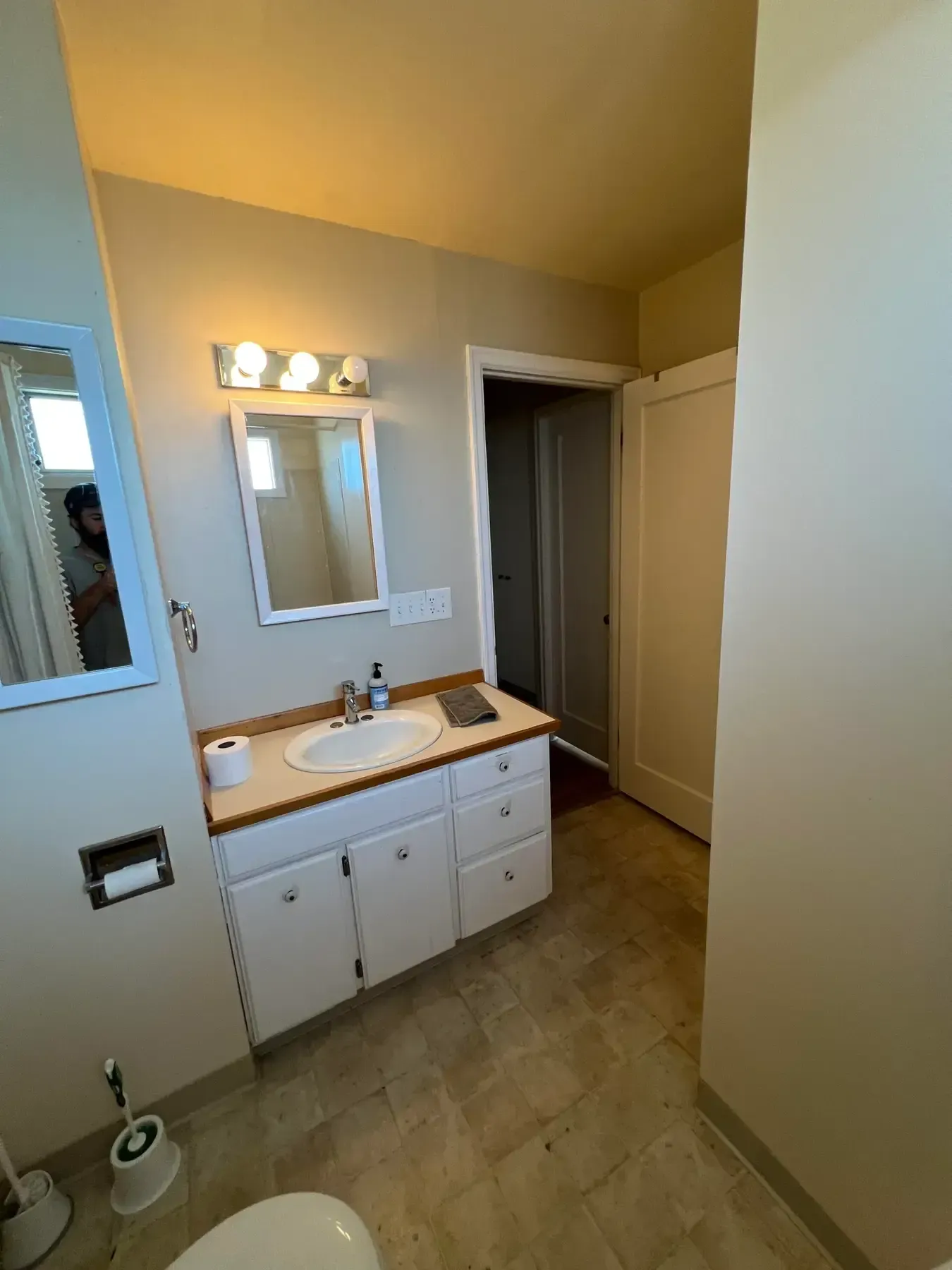Bathroom vanity with mirror, sink, lights, and an open doorway in a beige room.