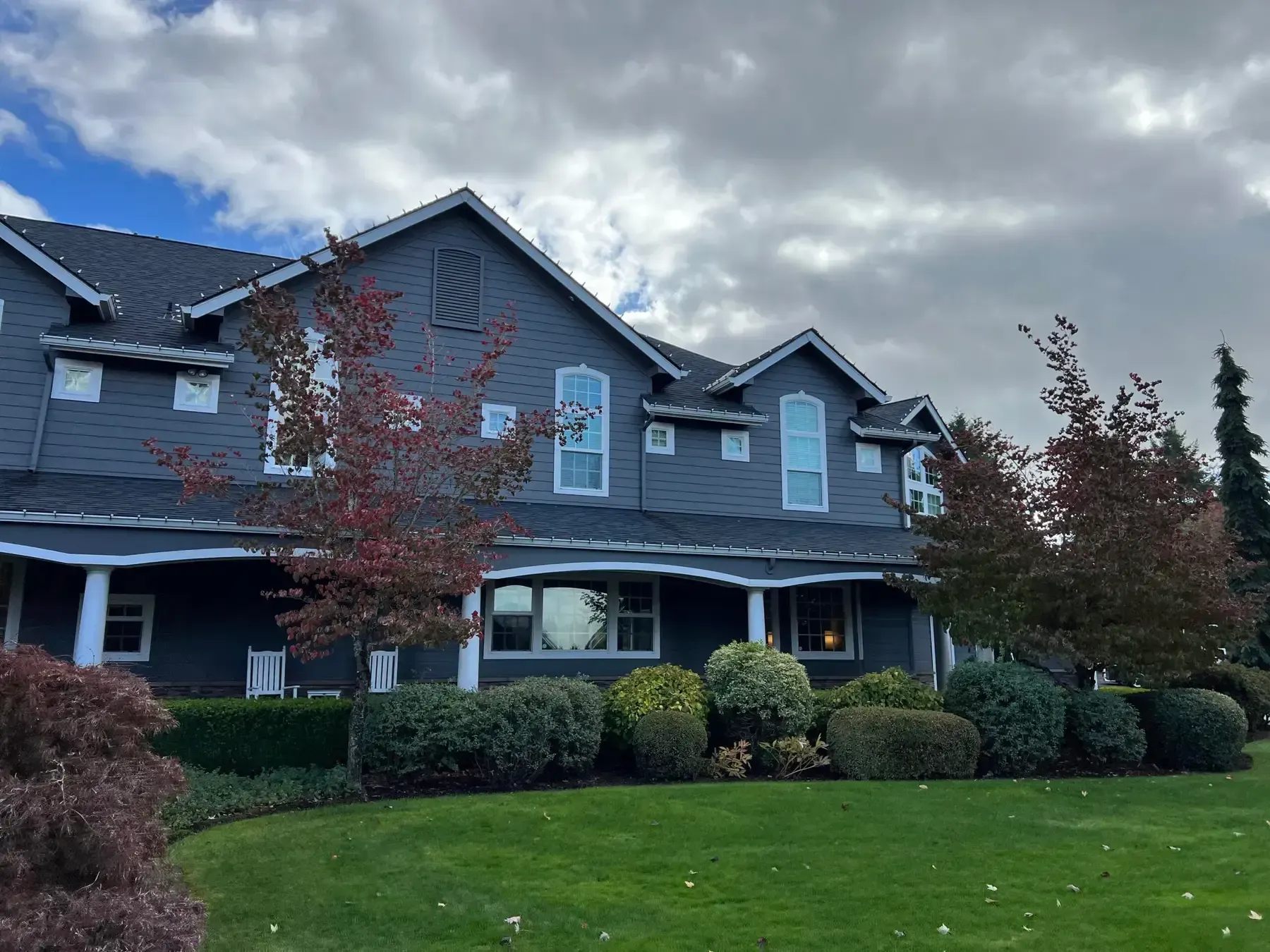 Blue-gray suburban house with white trim, front porch, and manicured lawn under cloudy skies