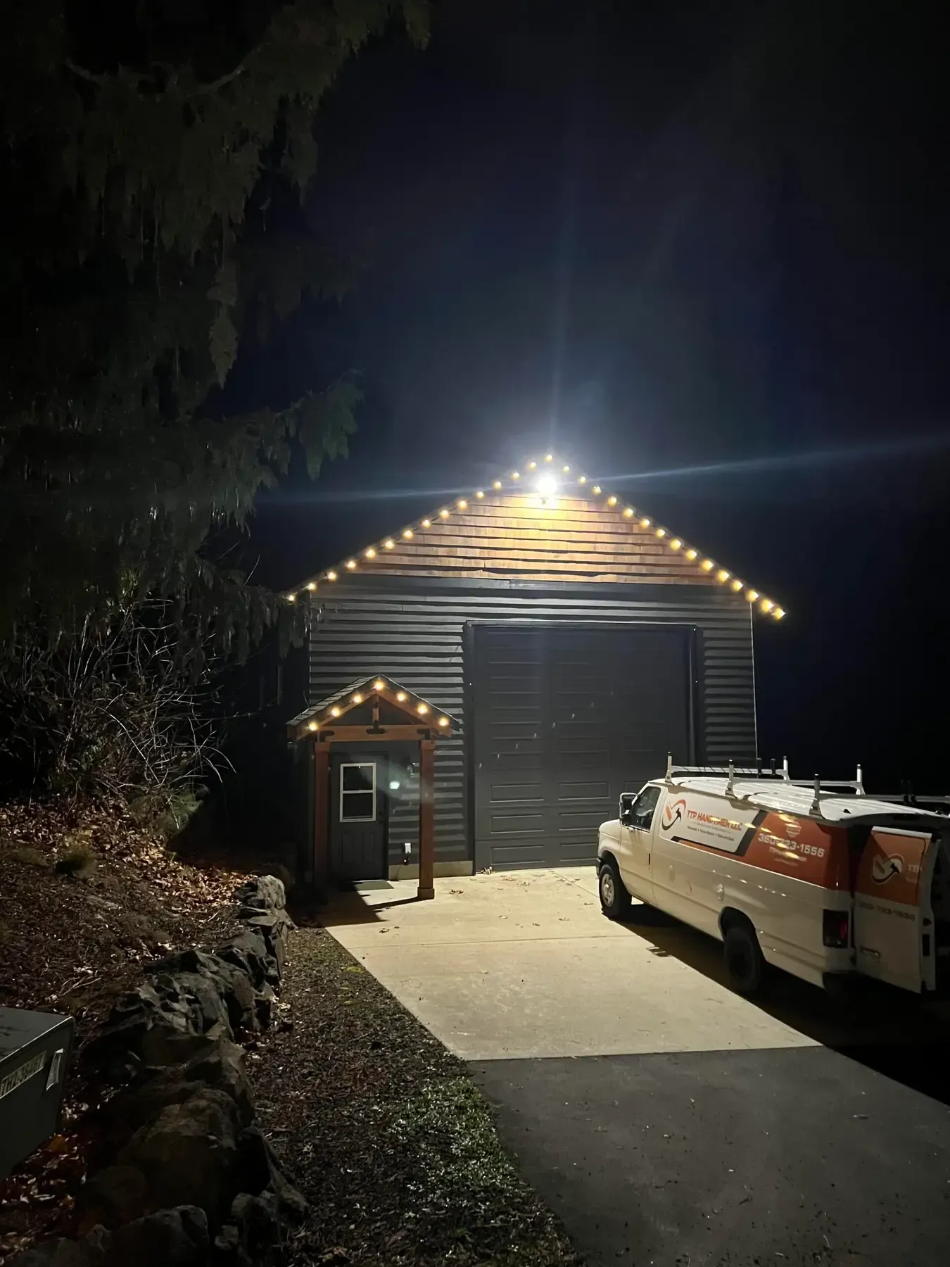 Nighttime view of a lit shed with a white utility truck parked beside a driveway.