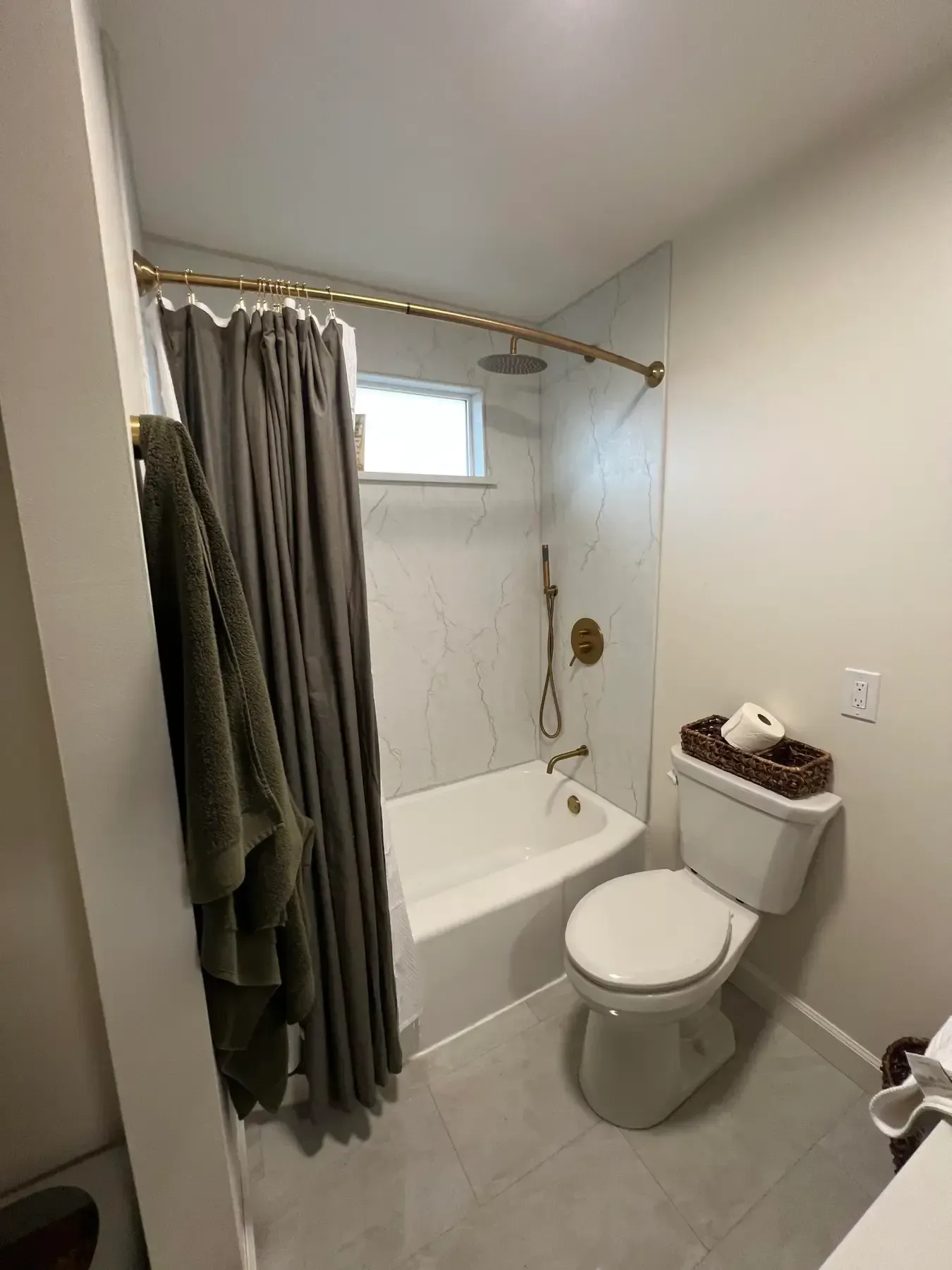 Small bathroom with shower curtain, bathtub, toilet, and window.