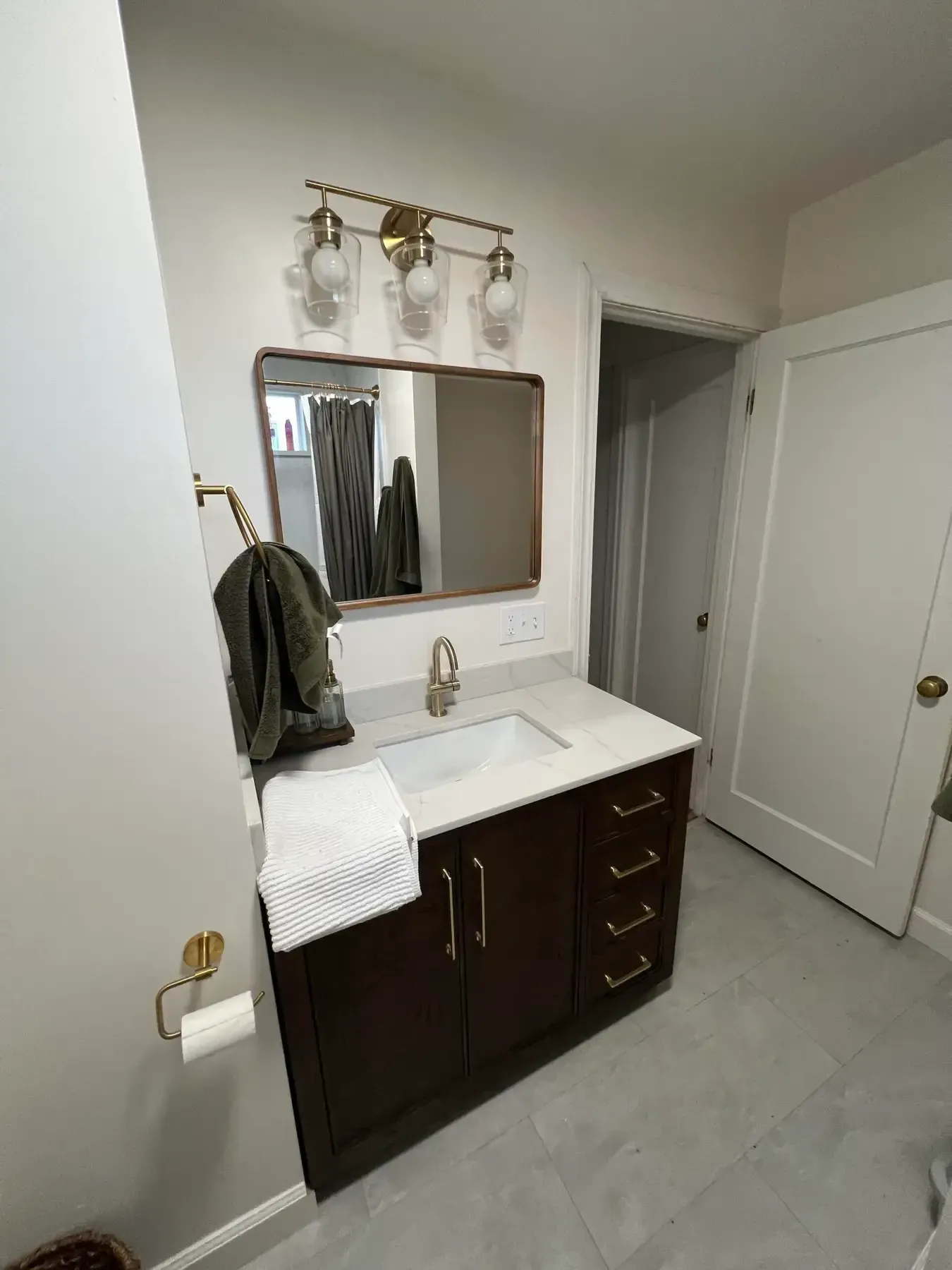 Bathroom vanity with dark wood cabinets, white countertop, mirror, and wall sconce lighting.
