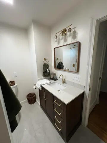 Small bathroom vanity with mirror, white countertop, dark cabinets, and hanging light fixture.