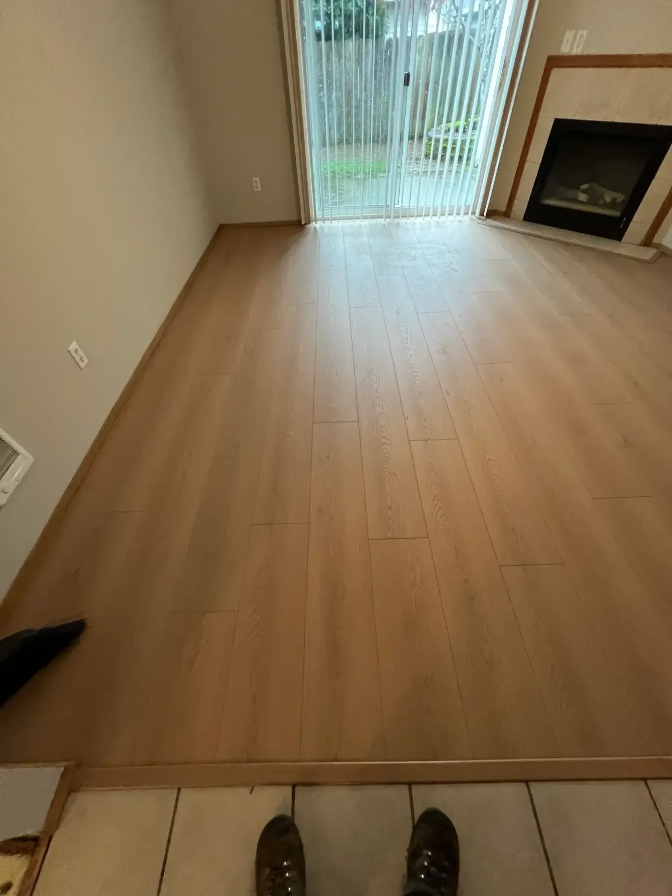 Empty living room with light wood floor, sliding glass doors, and a fireplace on the right.
