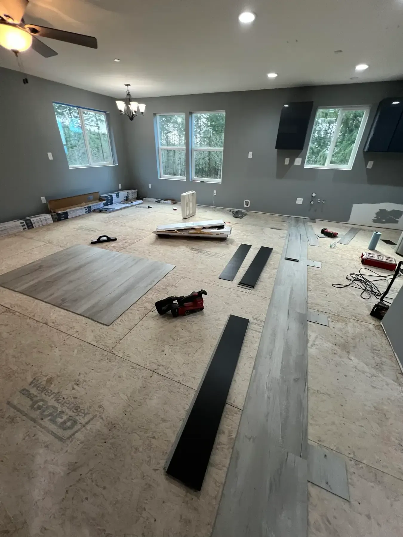 Living room renovation with floor underlayment, wood planks, tools, and windows.