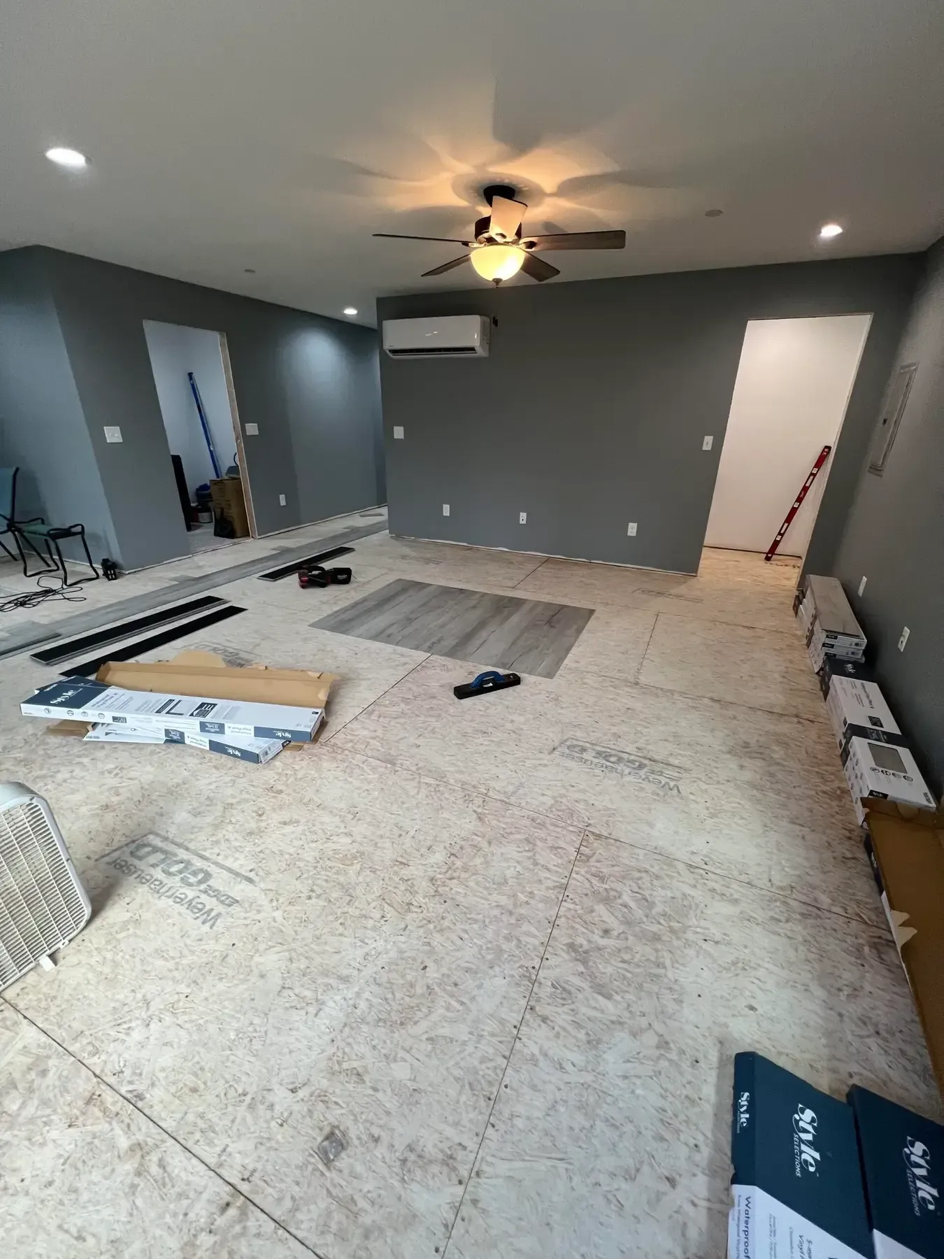 Empty gray room under renovation with scattered flooring materials and tools on the floor
