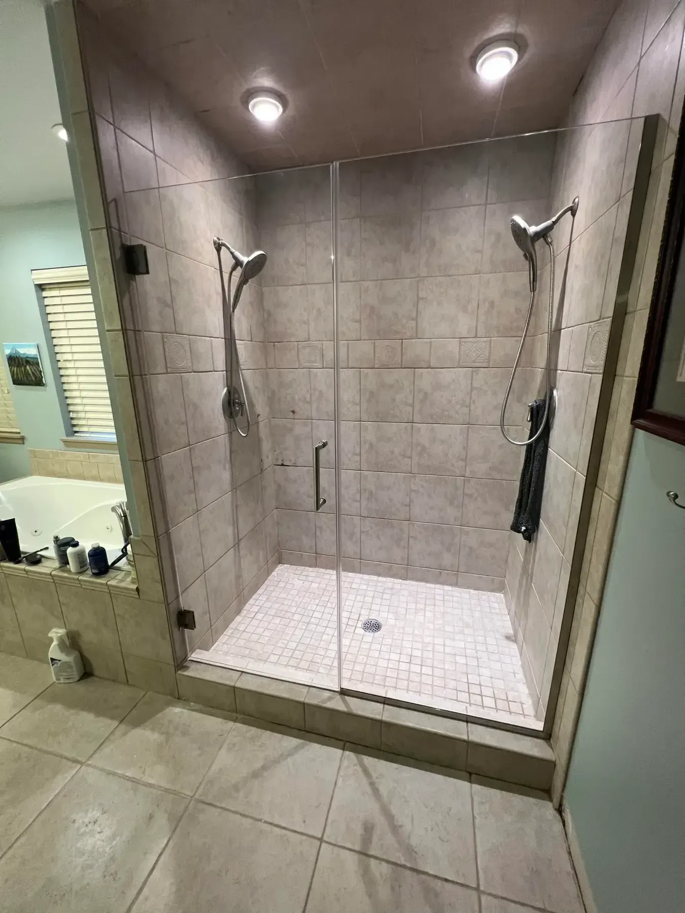 Walk-in shower with beige tile walls, two showerheads, and a white pebble-style shower floor
