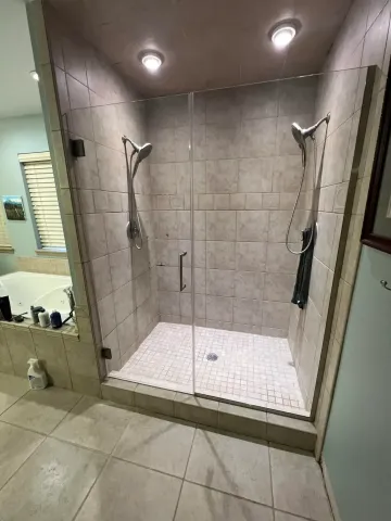 Accessible walk-in shower with two rain showerheads, tiled walls, and a low curb in a modern bathroom.