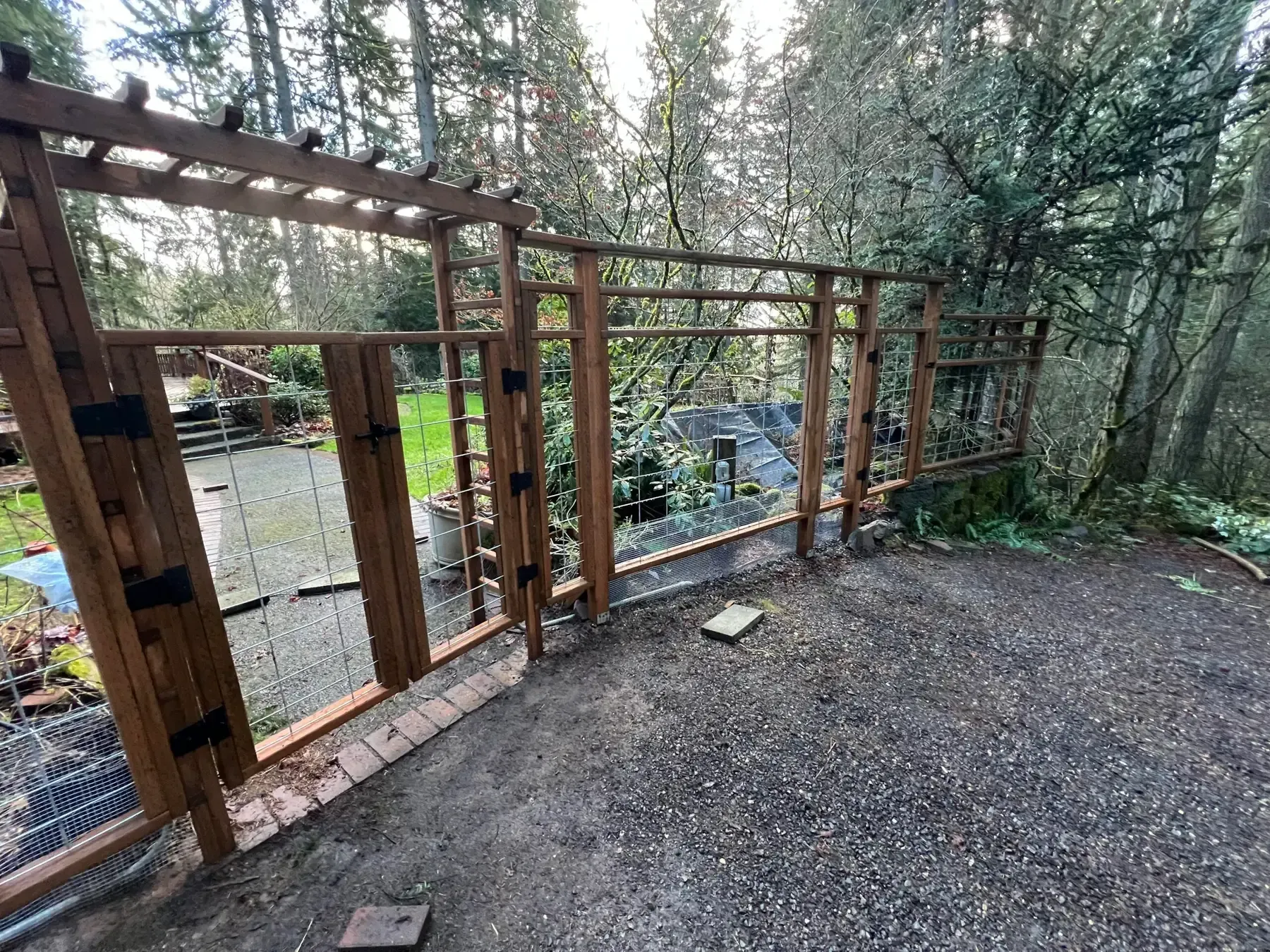 Wooden deck framing along a forested riverbank, with gravel ground and trees in the background.
