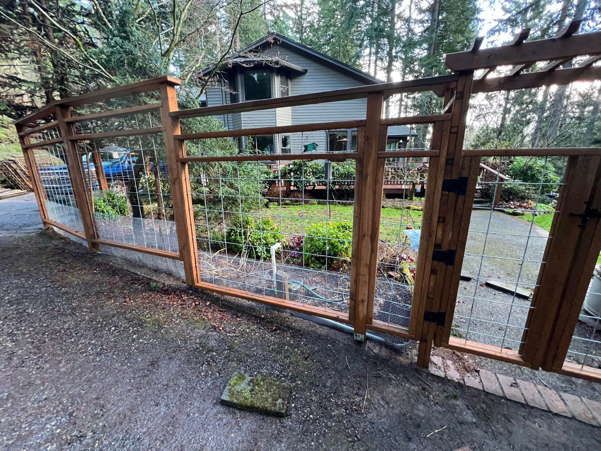 Wooden gate fence beside a driveway, with a house and garden behind it