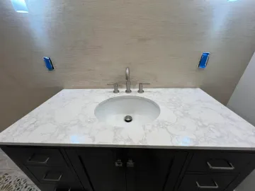 Bathroom vanity with white marble countertop, round sink, and dark cabinets against a beige wall.