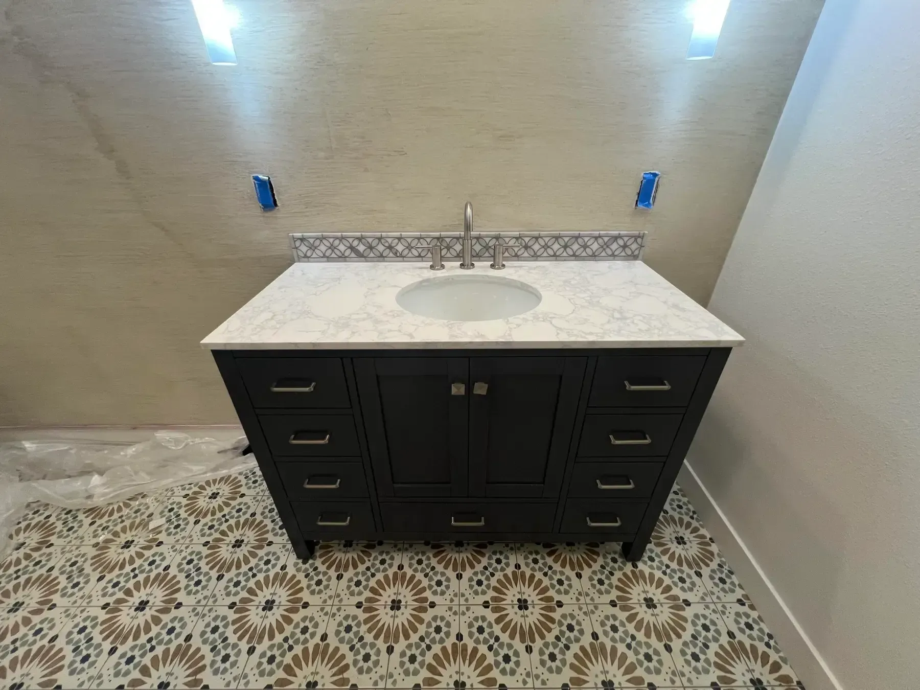 Modern bathroom vanity with white countertop, black cabinets, patterned floor tile, and beige walls