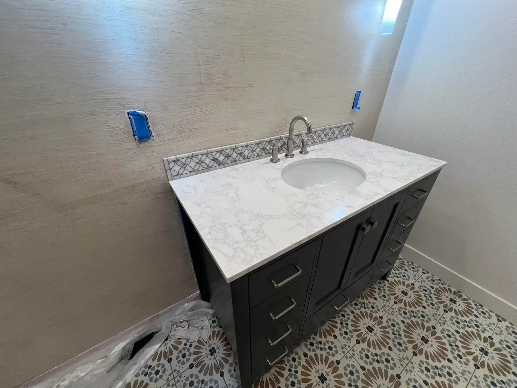 Bathroom vanity with white countertop, sink, chrome faucet, and dark cabinets in a tiled room