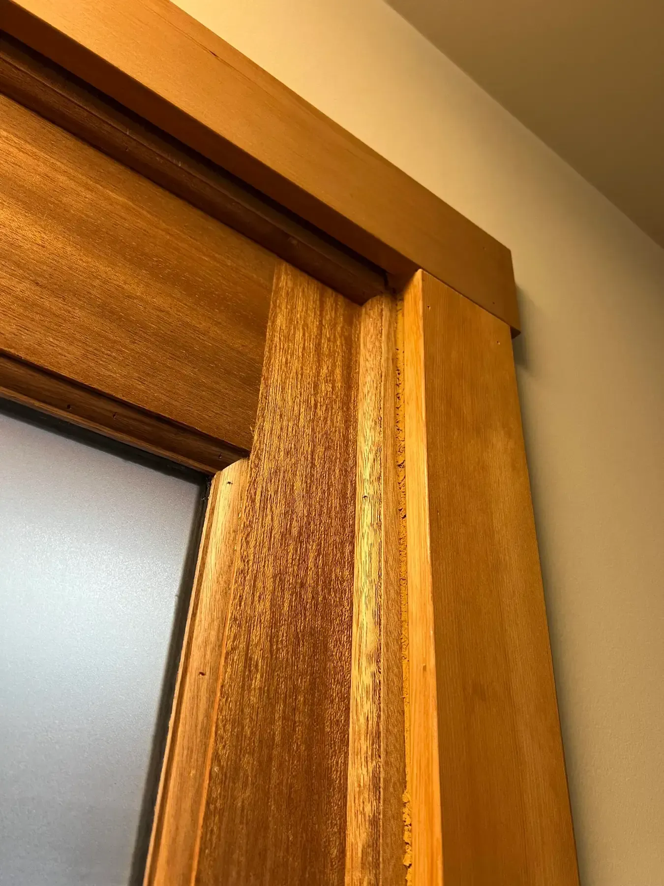 Close-up of a wooden door frame with beige curtain and frosted glass panel
