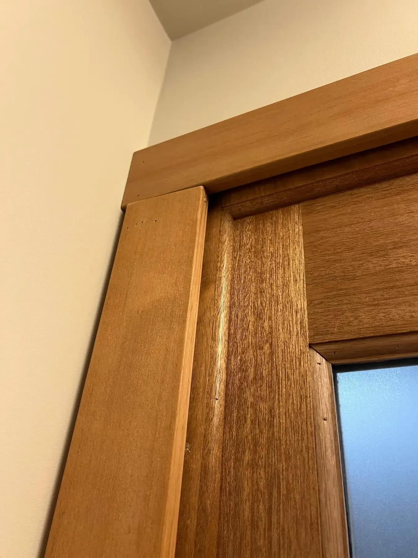 Close-up of a wooden door frame and corner of a wall, with a blue-tinted window or glass panel.
