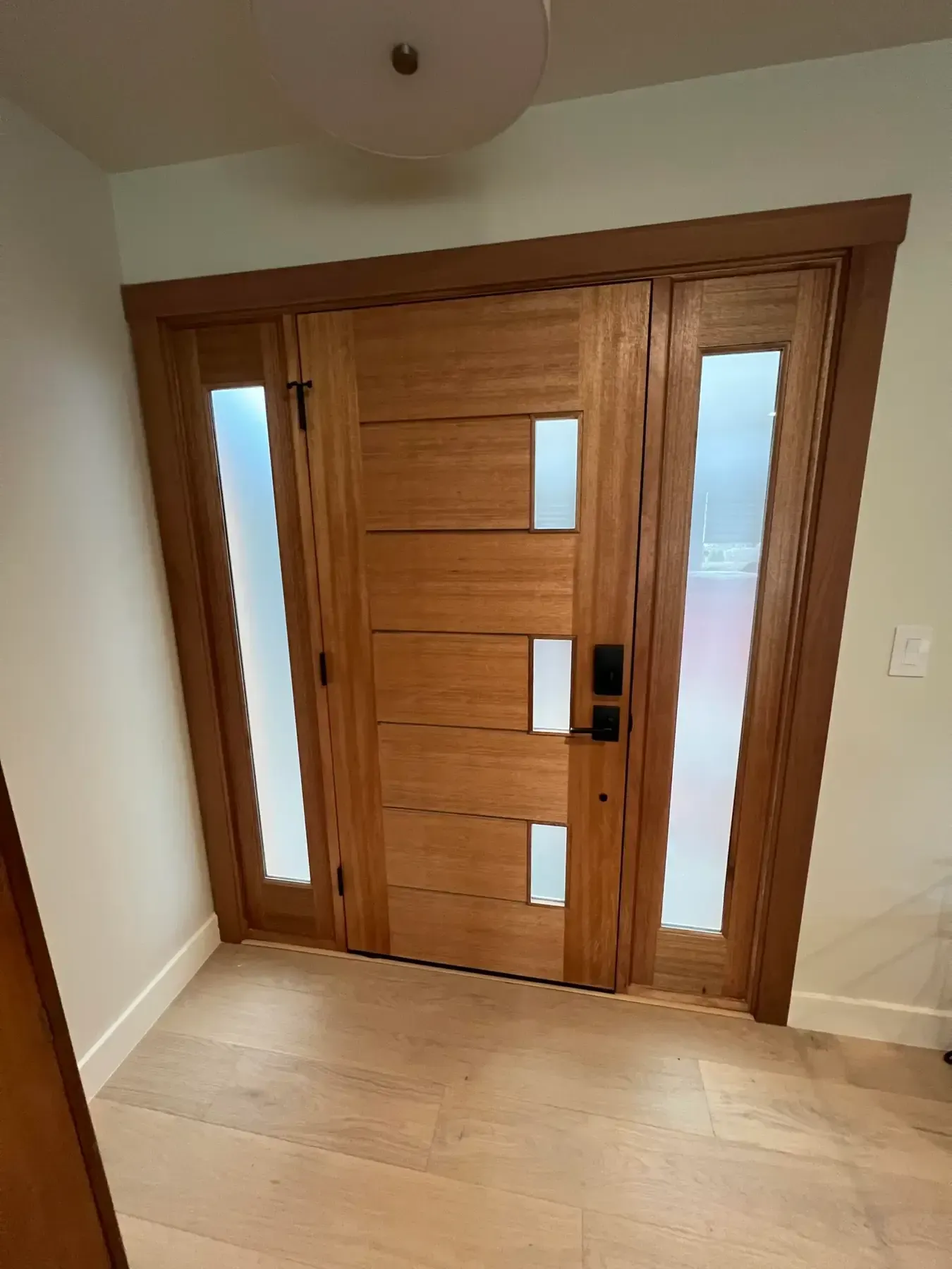 Wooden front door with narrow glass panels in a beige entryway