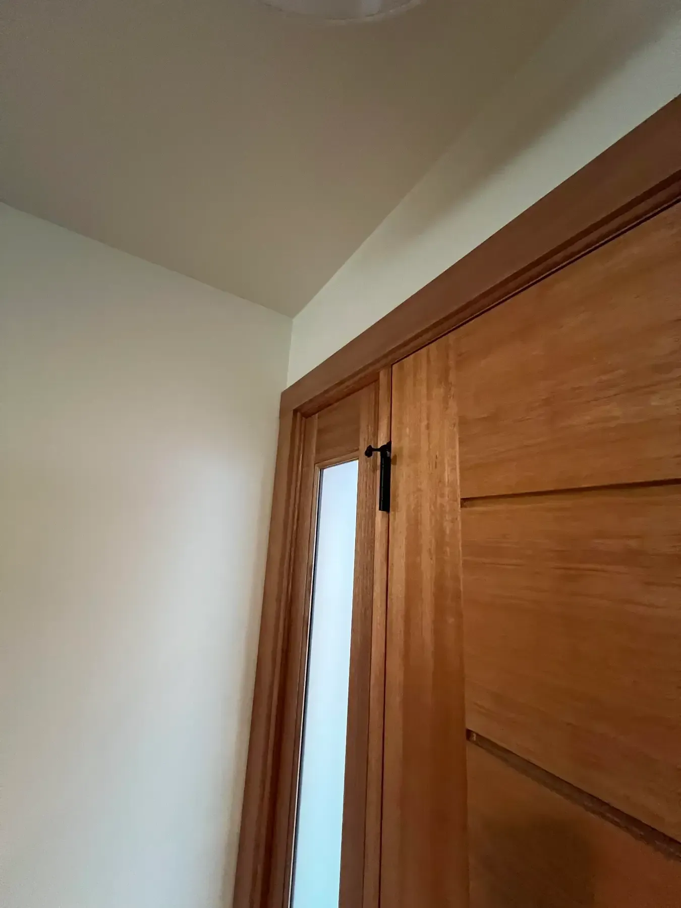 Wooden closet door with a narrow frosted-glass panel in a corner of a white room