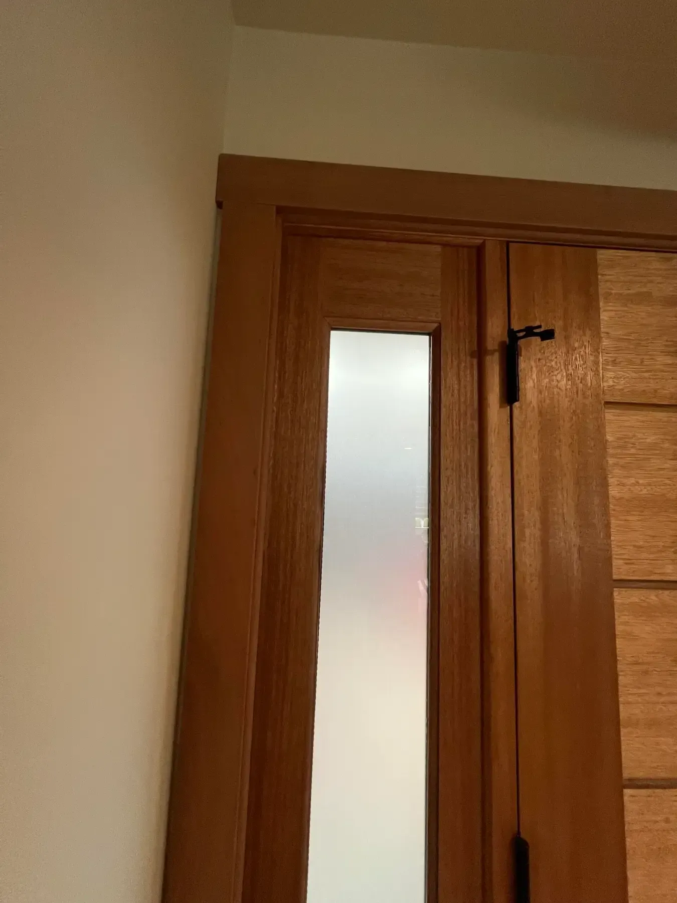 Wooden door with frosted glass panel slightly open against a beige wall.