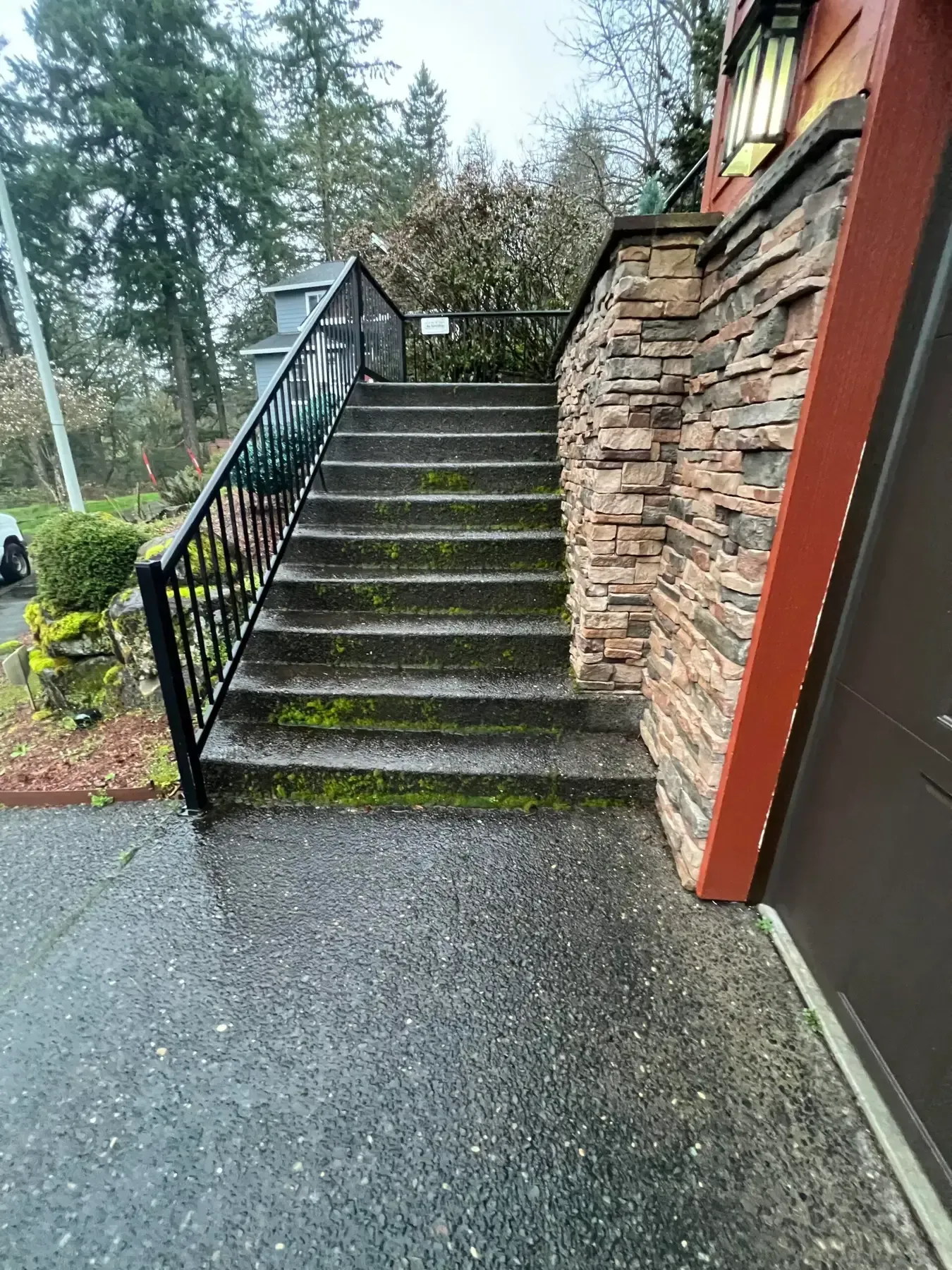Mossy outdoor staircase beside a stone wall and black railing on a wet walkway.