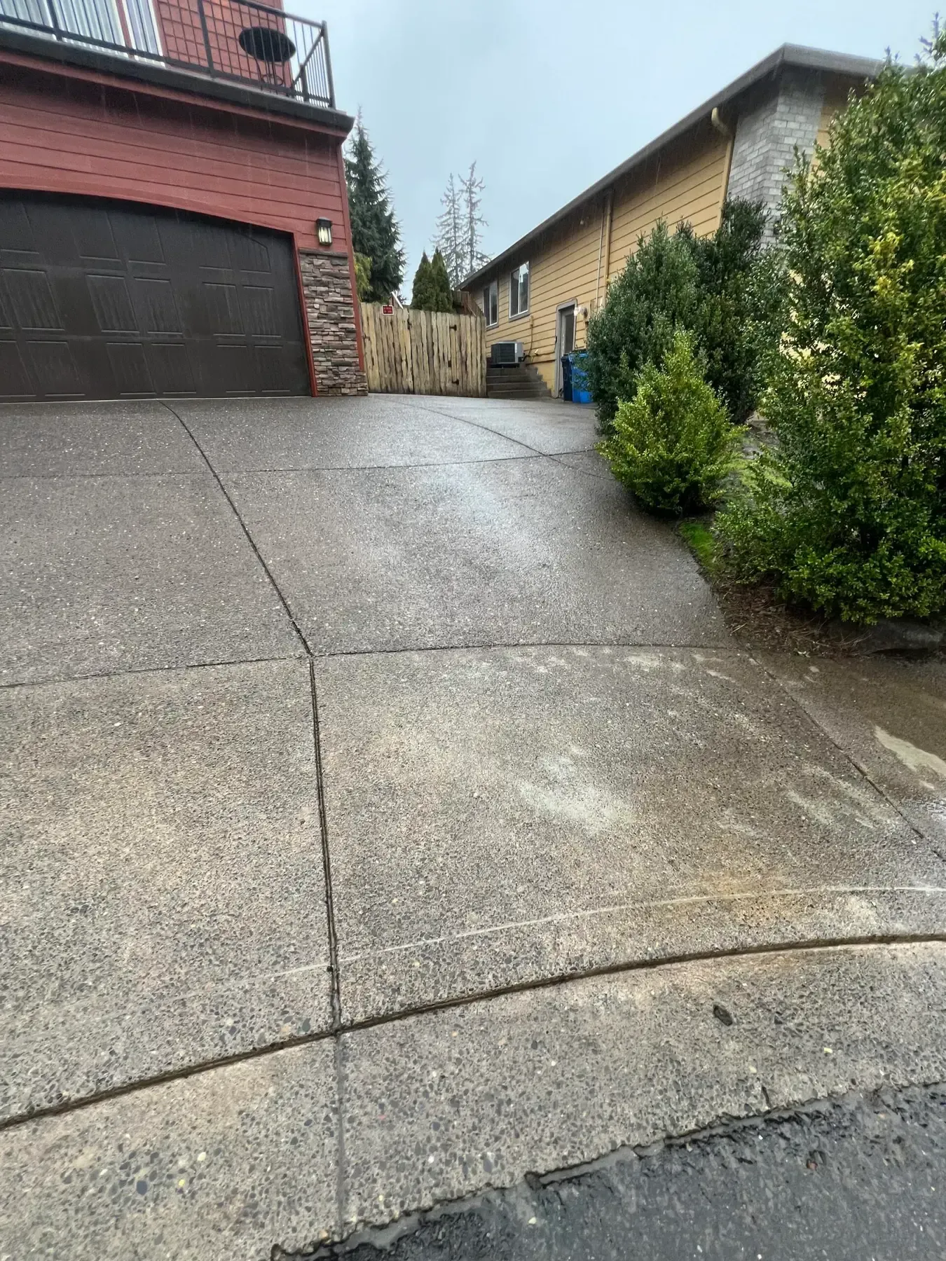 Steep wet driveway beside a brick garage and hedge-lined houses on a rainy day