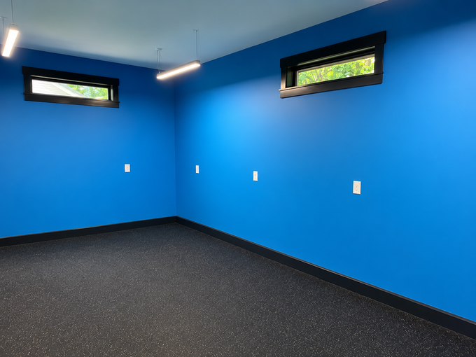 Empty blue room with black speckled floor and narrow windows near the ceiling