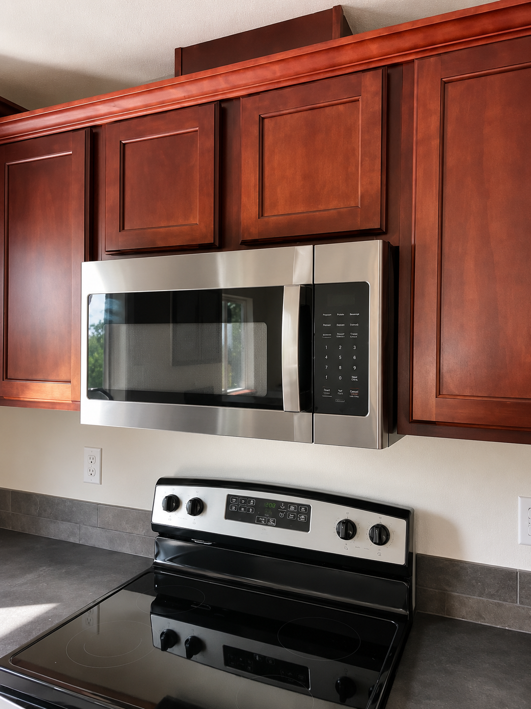 Kitchen stove with stainless steel microwave and dark wood cabinets above a black countertop.