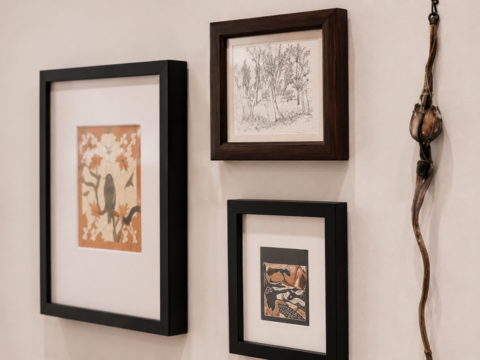 Three framed artworks and a wall hanging on a beige wall.
