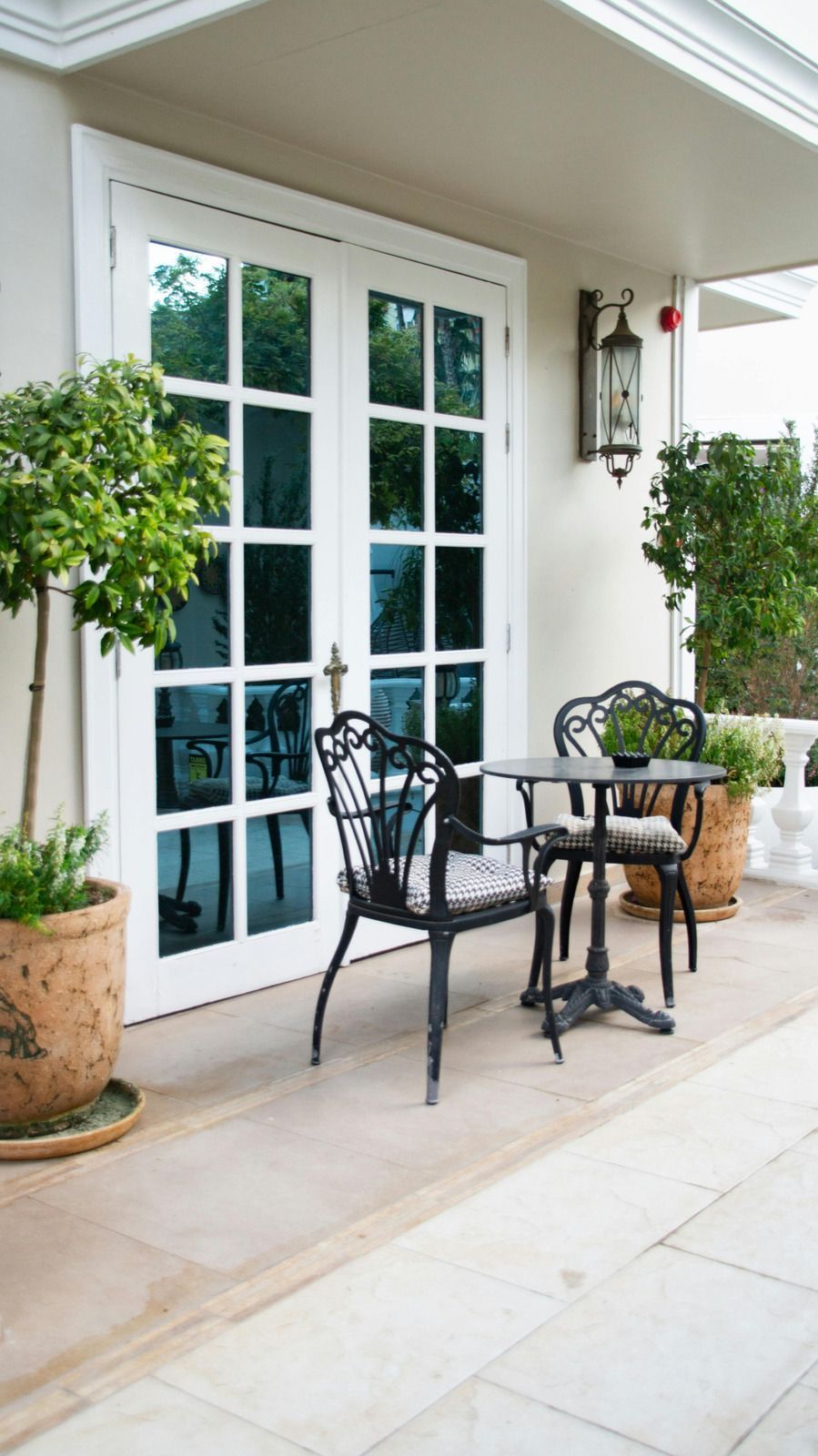 White French doors beside a small black bistro table and chairs on a covered patio with potted plants