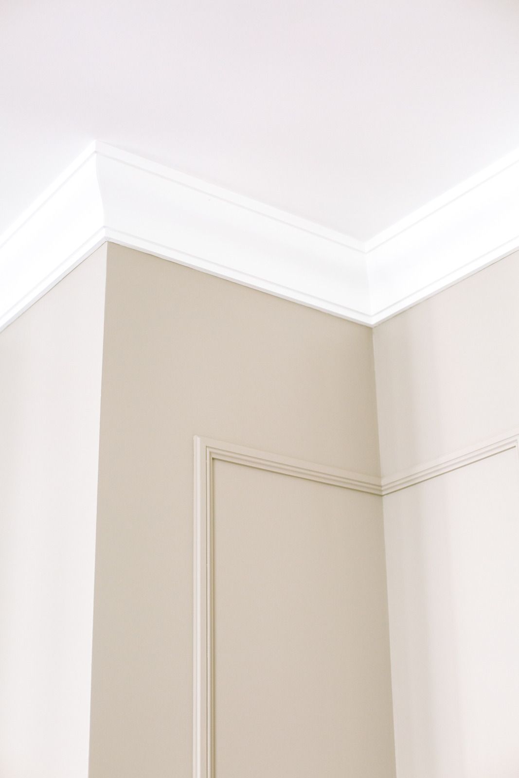 Corner of a beige room with white crown molding and a closed door trim piece