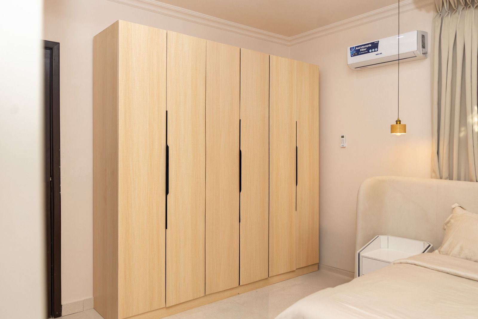 Minimal bedroom with light wood wardrobe, bed, and wall-mounted air conditioner