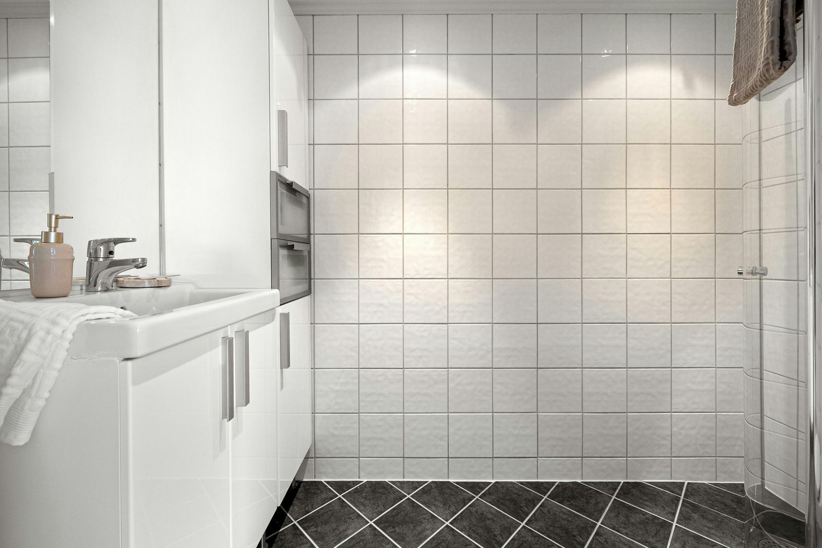 Bright white bathroom with tiled shower wall, vanity sink, and dark patterned floor