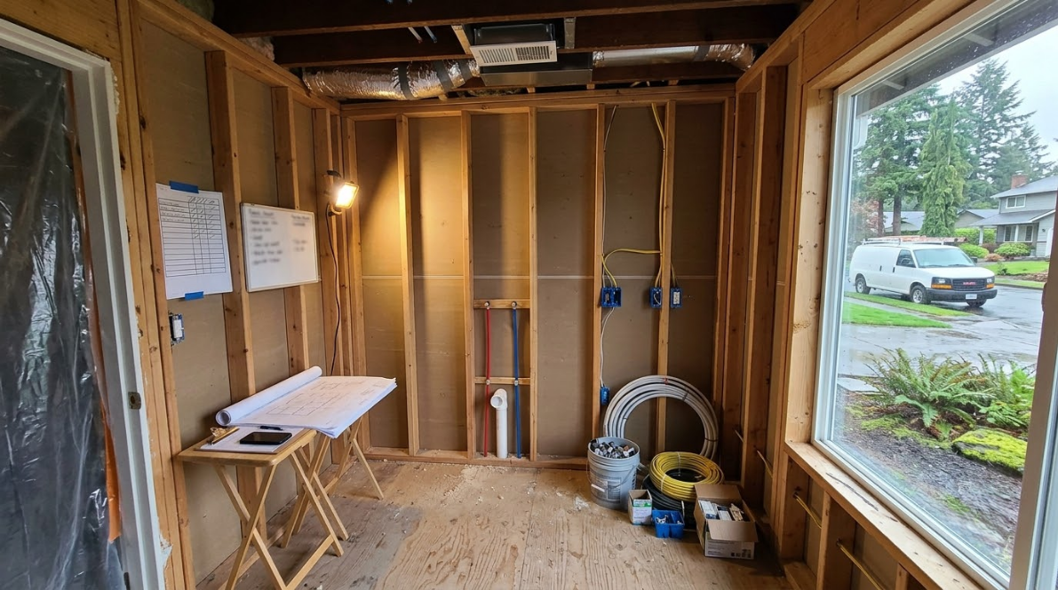 Unfinished room with exposed framing, workbench, tools, and a large window overlooking a street.