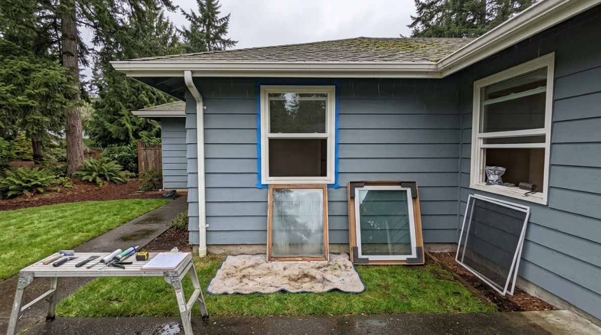 Blue house exterior with a small porch, potted plants, and leaning window screens by the wall